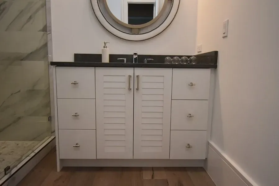 White bathroom vanity with dark countertop, round mirror, and wood floor.