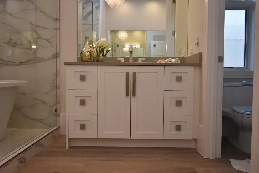 White bathroom vanity with drawers and doors, gray countertop, and large mirror.
