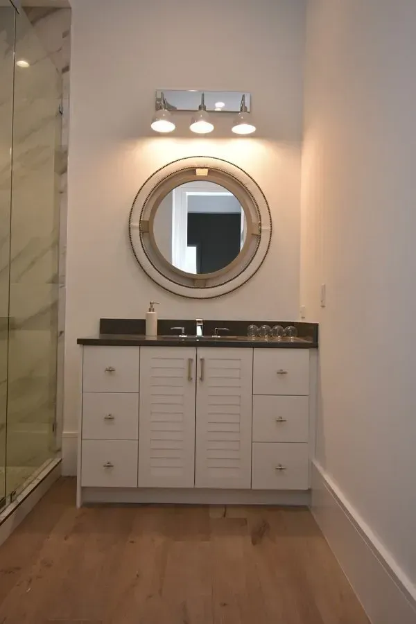Bathroom vanity with a round mirror, white cabinets, and chrome light fixture.