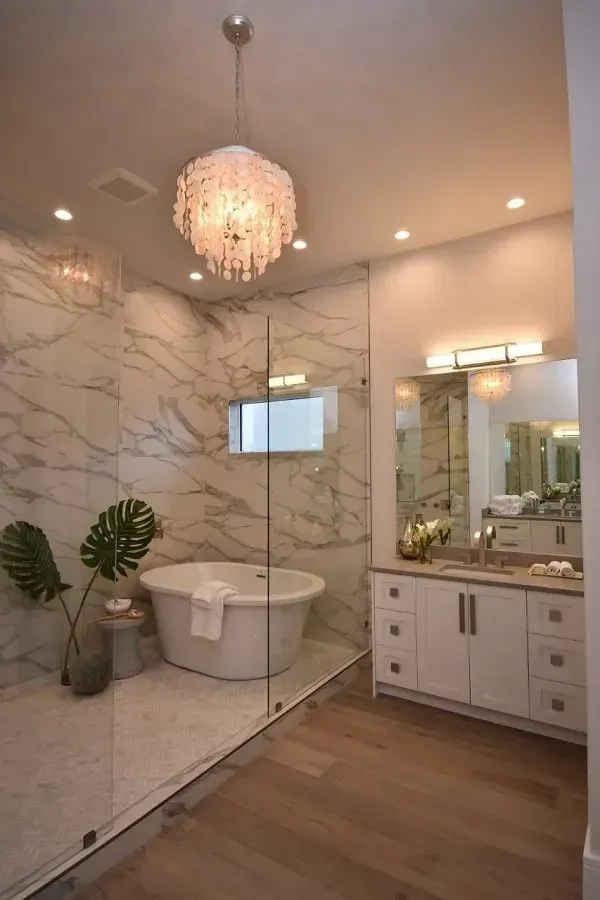 Luxurious bathroom with marble walls, freestanding tub, glass shower, and crystal chandelier.