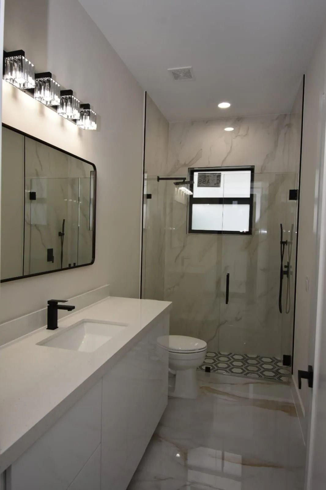 Modern white bathroom with marble accents, black fixtures, and glass shower.