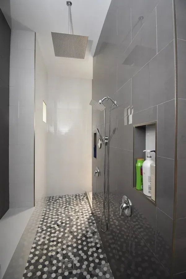 Modern shower with gray and white tile, rainfall showerhead, and mosaic floor.