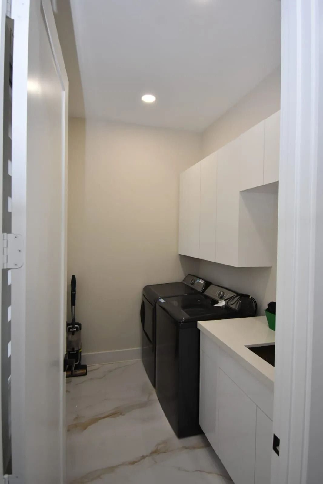 Laundry room with black washer and dryer, white cabinets, and marble-look tile flooring.