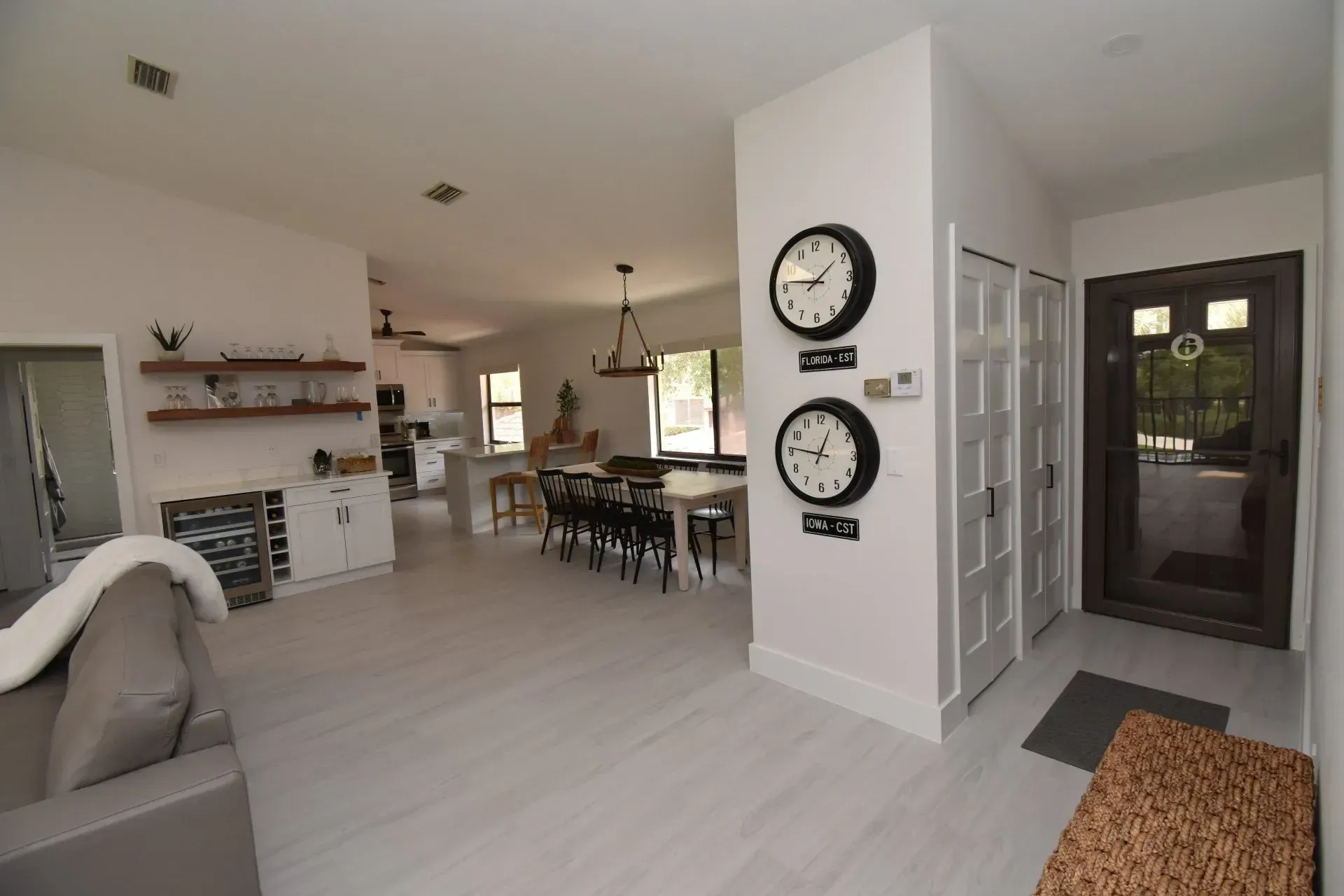 Spacious home interior with light gray flooring, open kitchen, dining area, and entryway with two clocks.