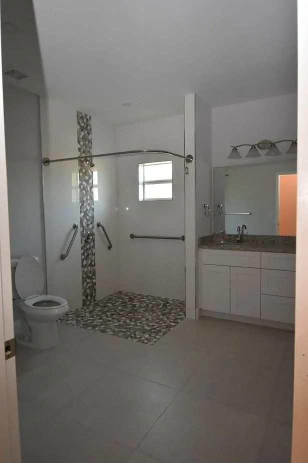 Accessible bathroom with a roll-in shower, grab bars, white cabinets, and a toilet.