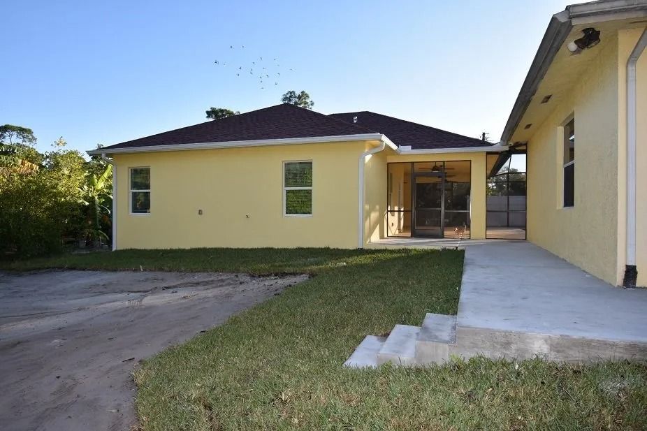 Yellow house with a brown roof and a concrete patio in the yard.