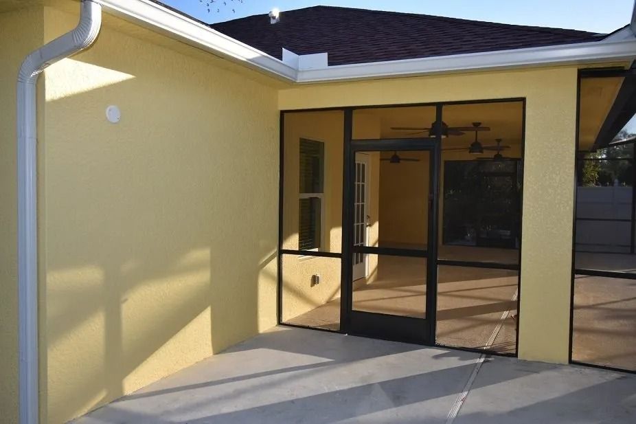 Yellow house exterior with screen-enclosed porch. Door and windows lead into the porch, with concrete flooring.