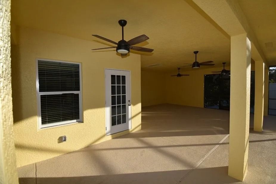 Covered patio with yellow walls, ceiling fans, door, window, and concrete floor.
