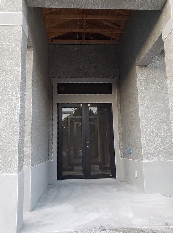 Exterior entryway with double doors beneath a porch roof, gray walls and accents.