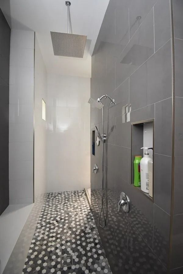 Modern walk-in shower with gray tile walls, white side wall, a mosaic tile floor, and overhead shower head.