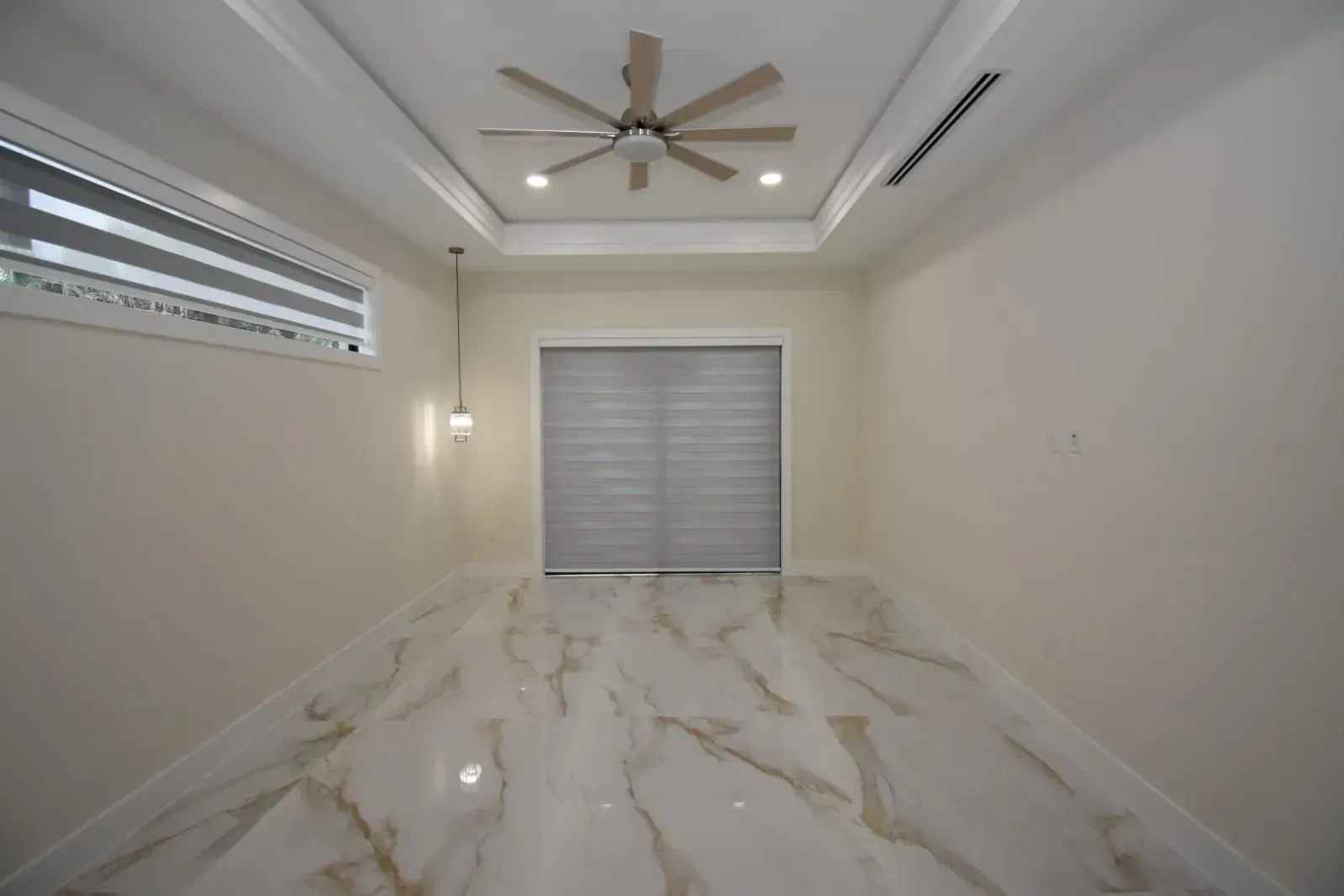 Empty room with light-colored walls and marble tile floor. Features include a window, ceiling fan, and closed window shades.