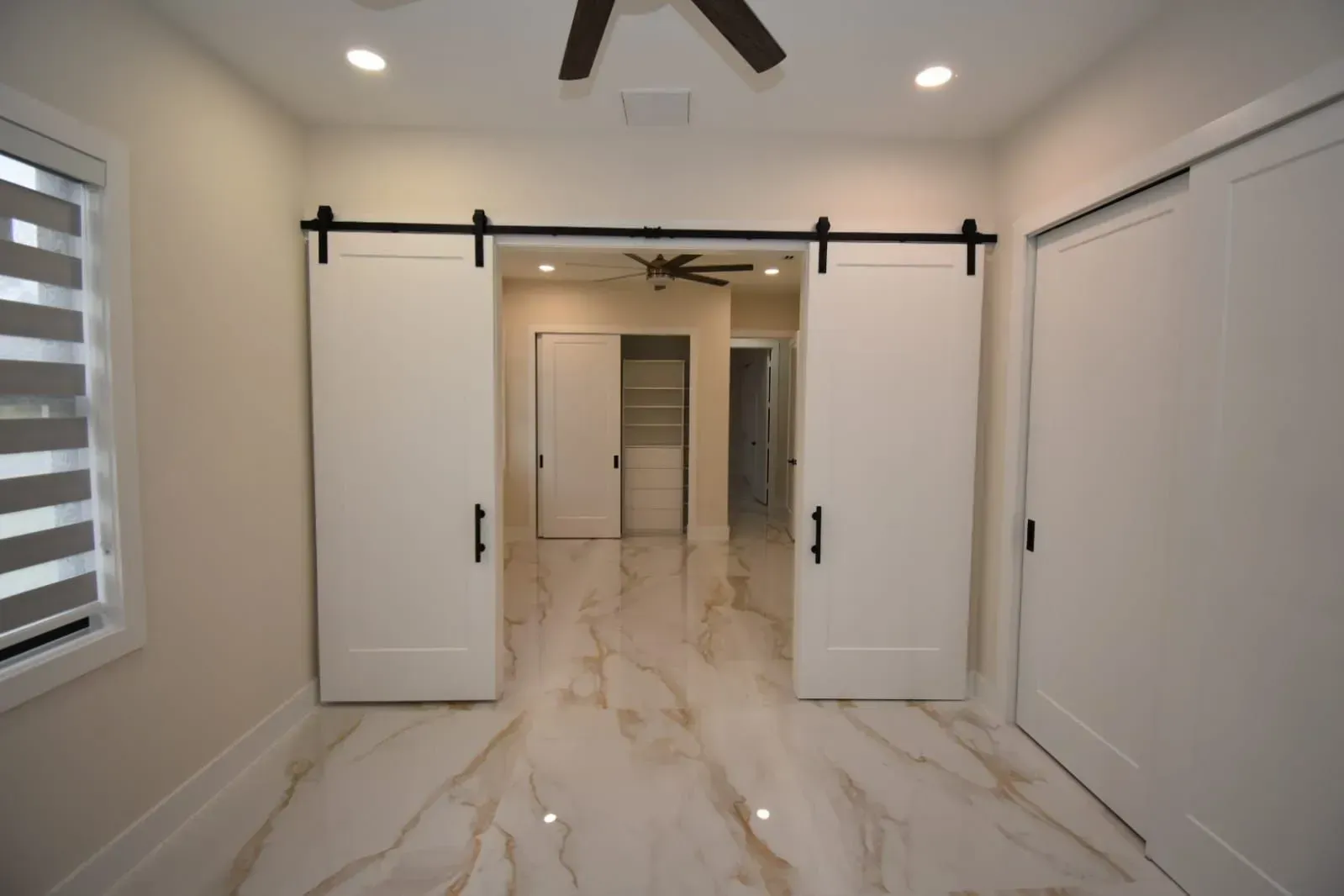Interior room with white sliding barn doors, beige marble floor, and recessed lighting.
