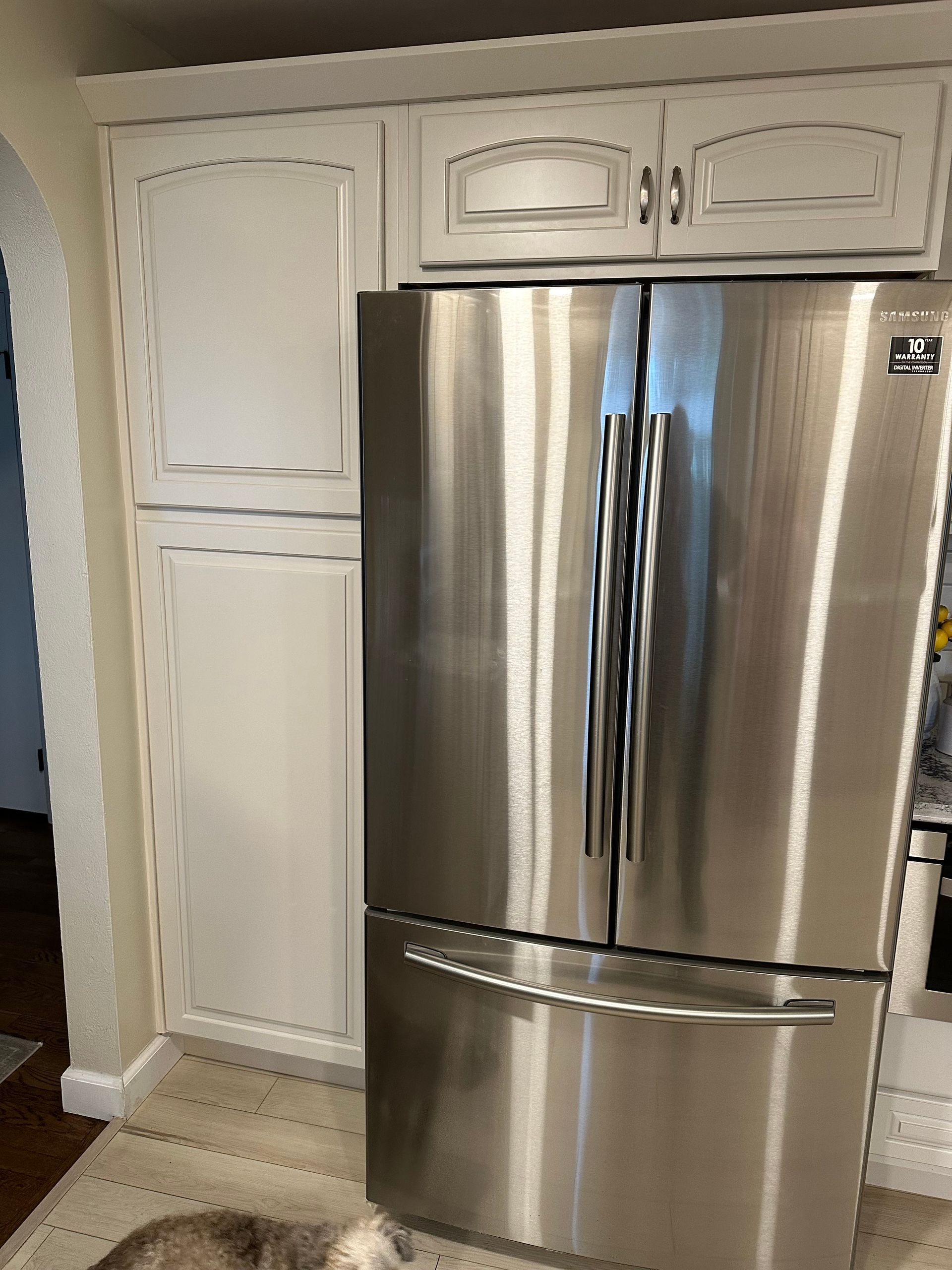Stainless steel refrigerator beside white kitchen cabinets in a bright kitchen.