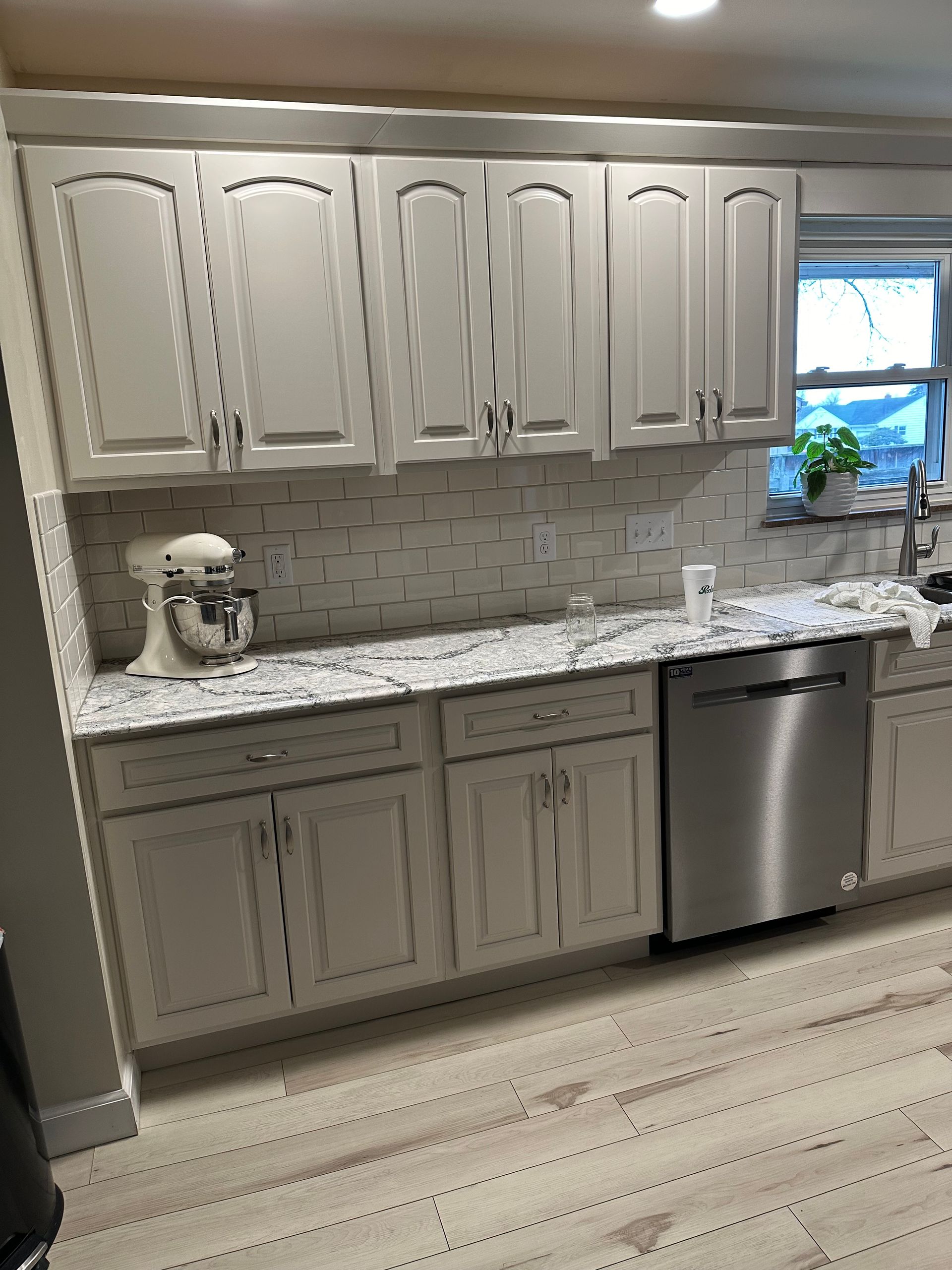 Modern kitchen with white cabinets, granite counters, subway tile backsplash, mixer, and stainless dishwasher.