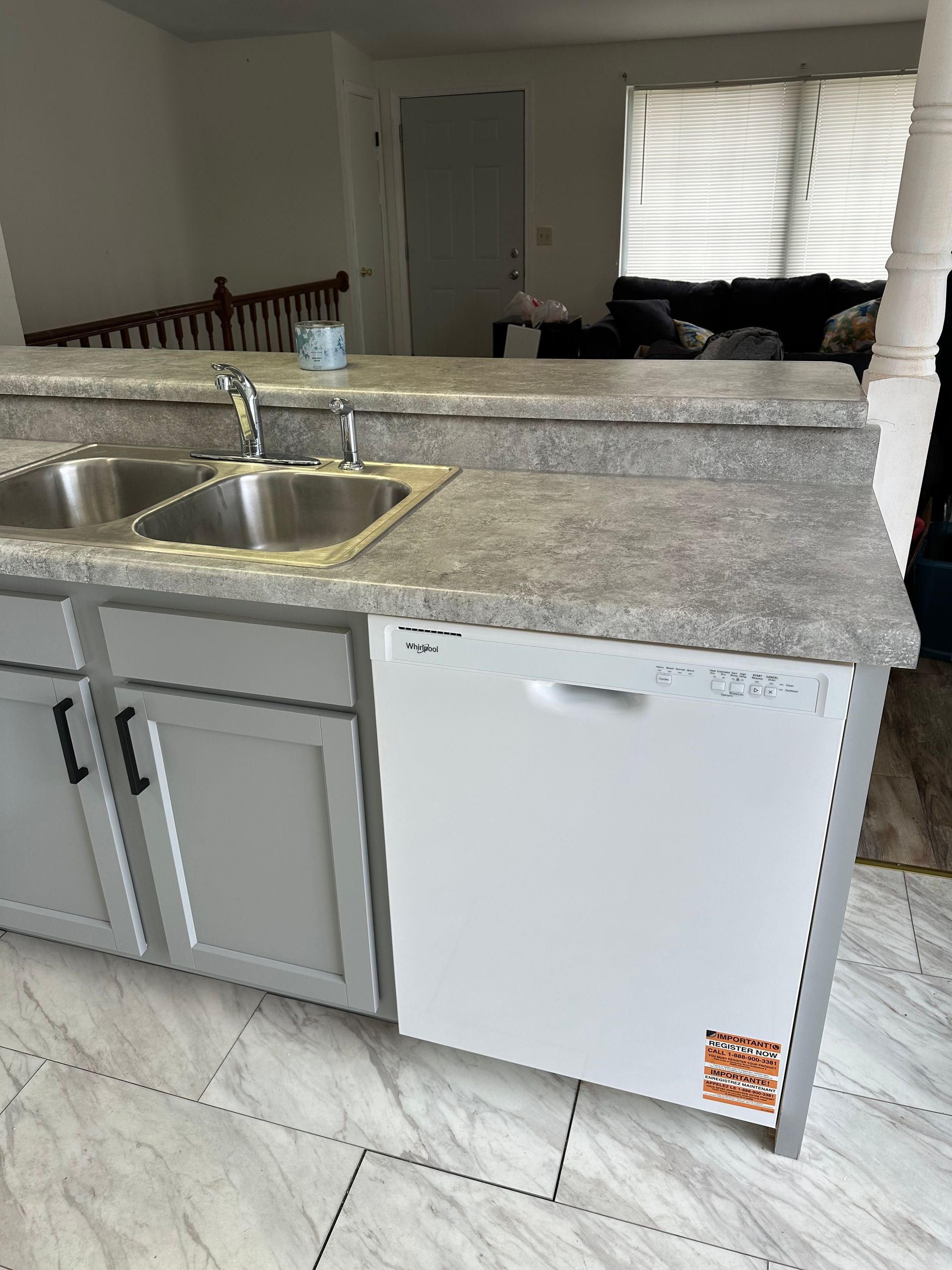 Kitchen island with stainless sink, granite countertop, gray cabinets, and a white dishwasher in an open room