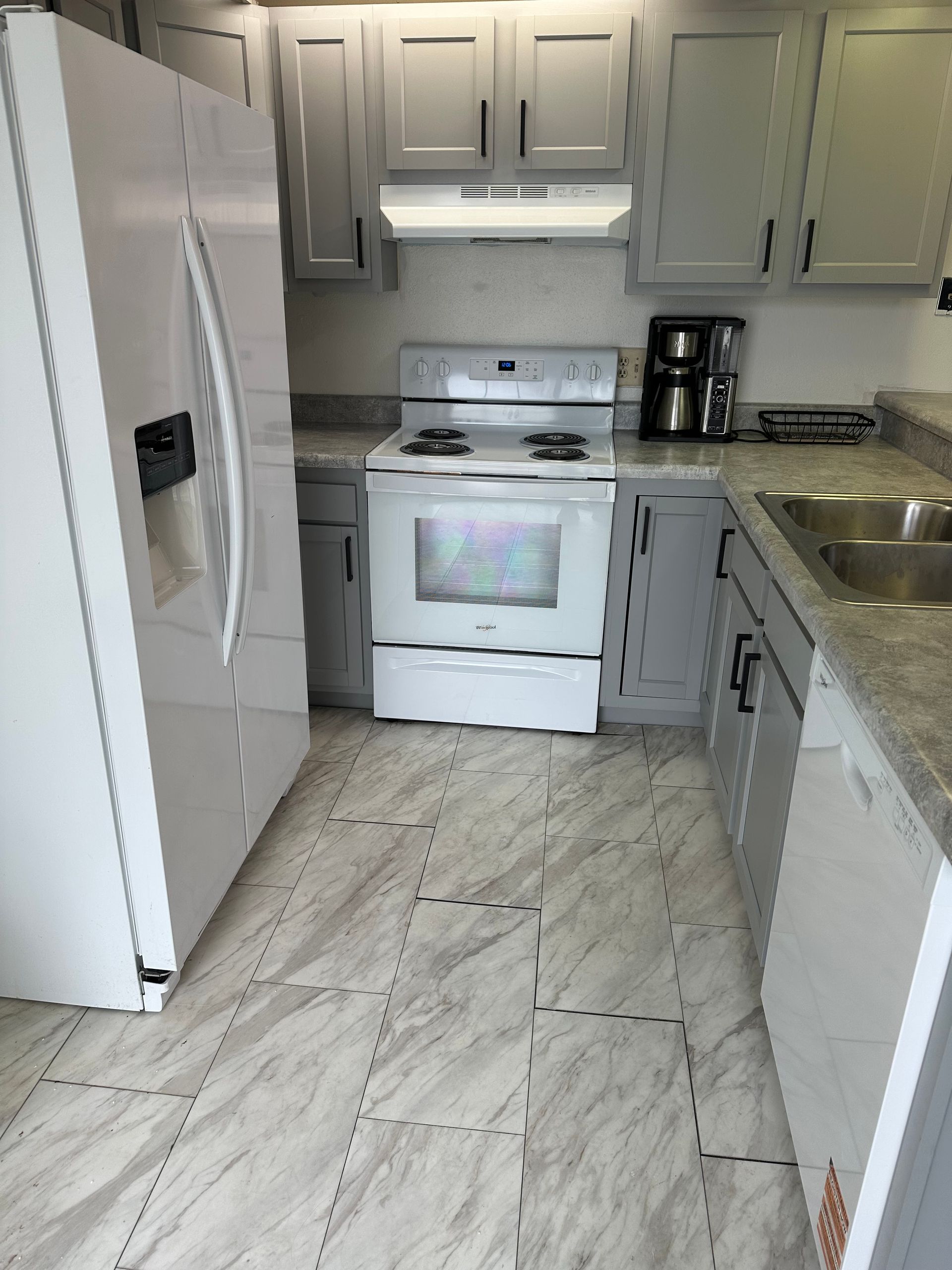 Small gray kitchen with white appliances, marble-look floor, and black coffee maker on the counter