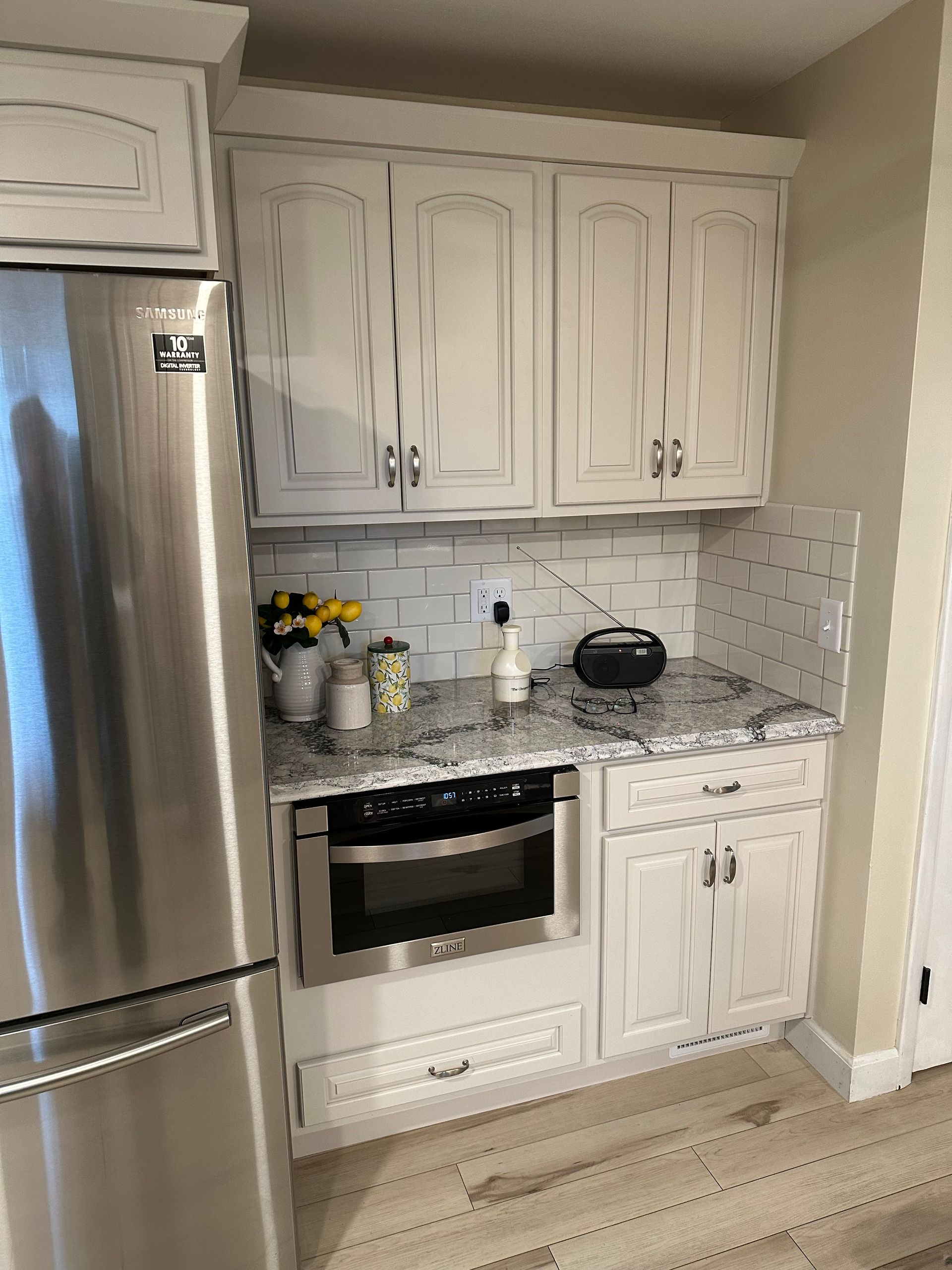 Small kitchen with white cabinets, stainless refrigerator, oven, and light wood flooring.