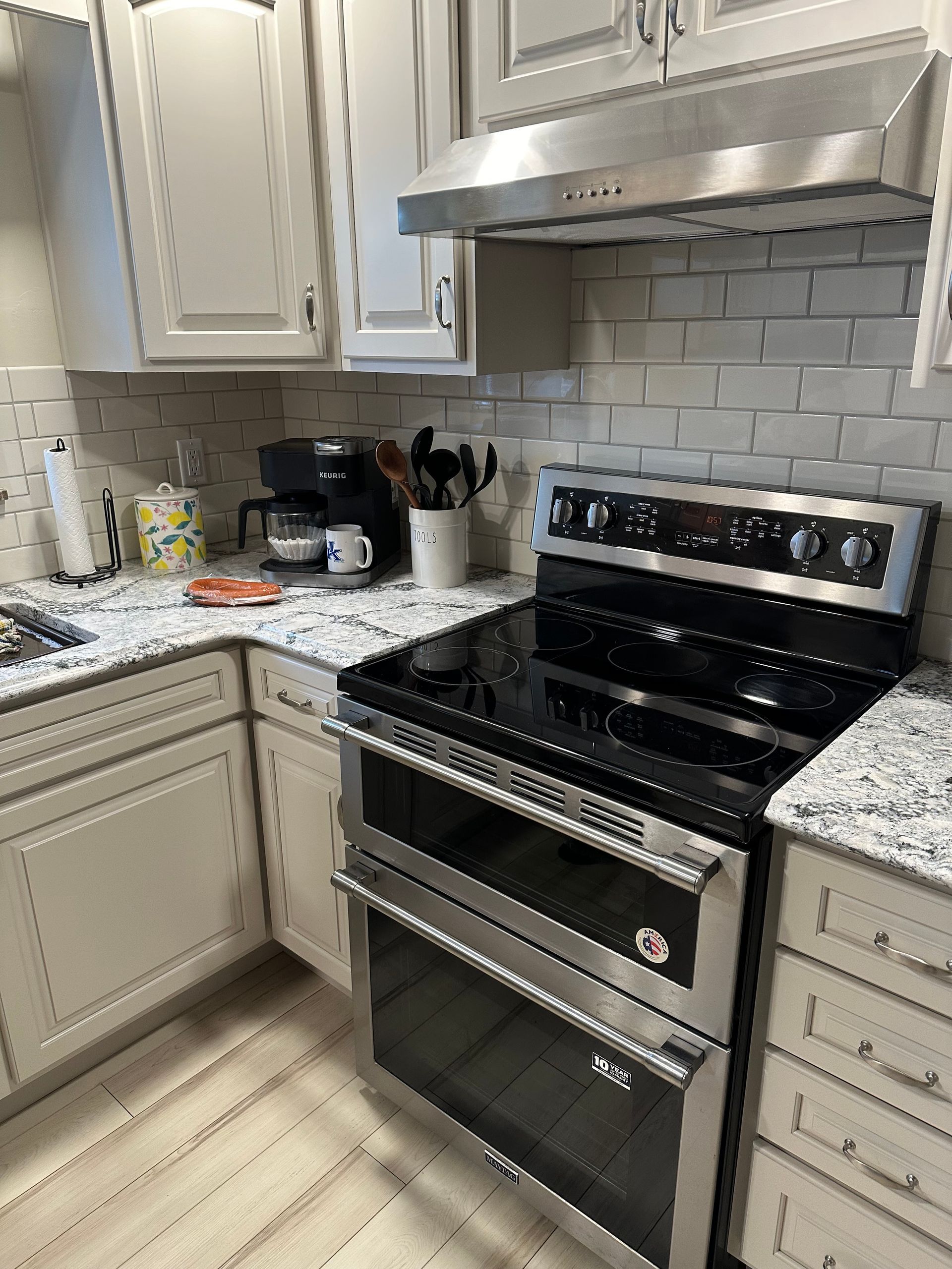 Modern kitchen with white cabinets, granite counters, and a stainless steel stove under a vent hood.