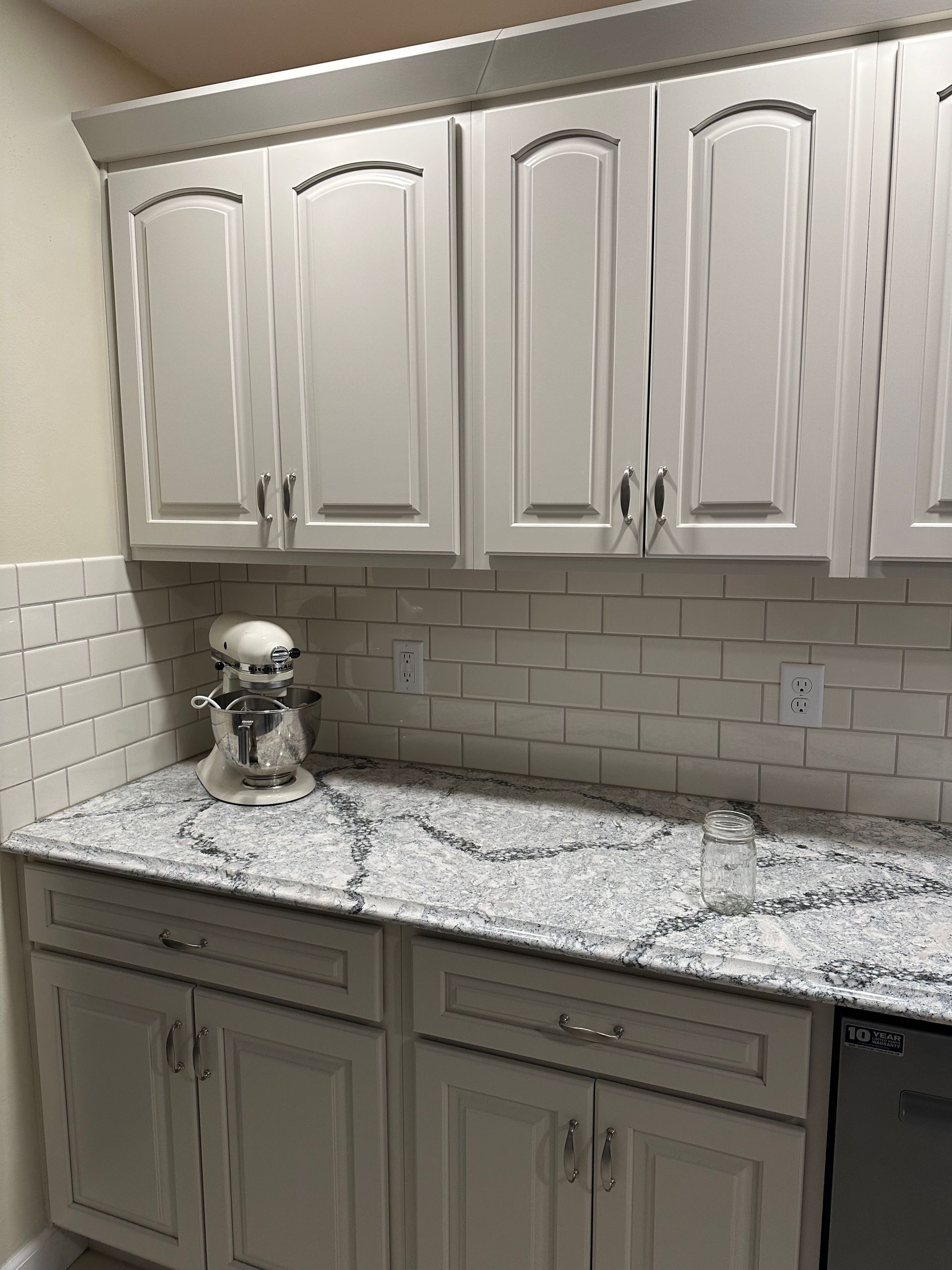 White kitchen cabinets and marble countertop with a stand mixer on the left.