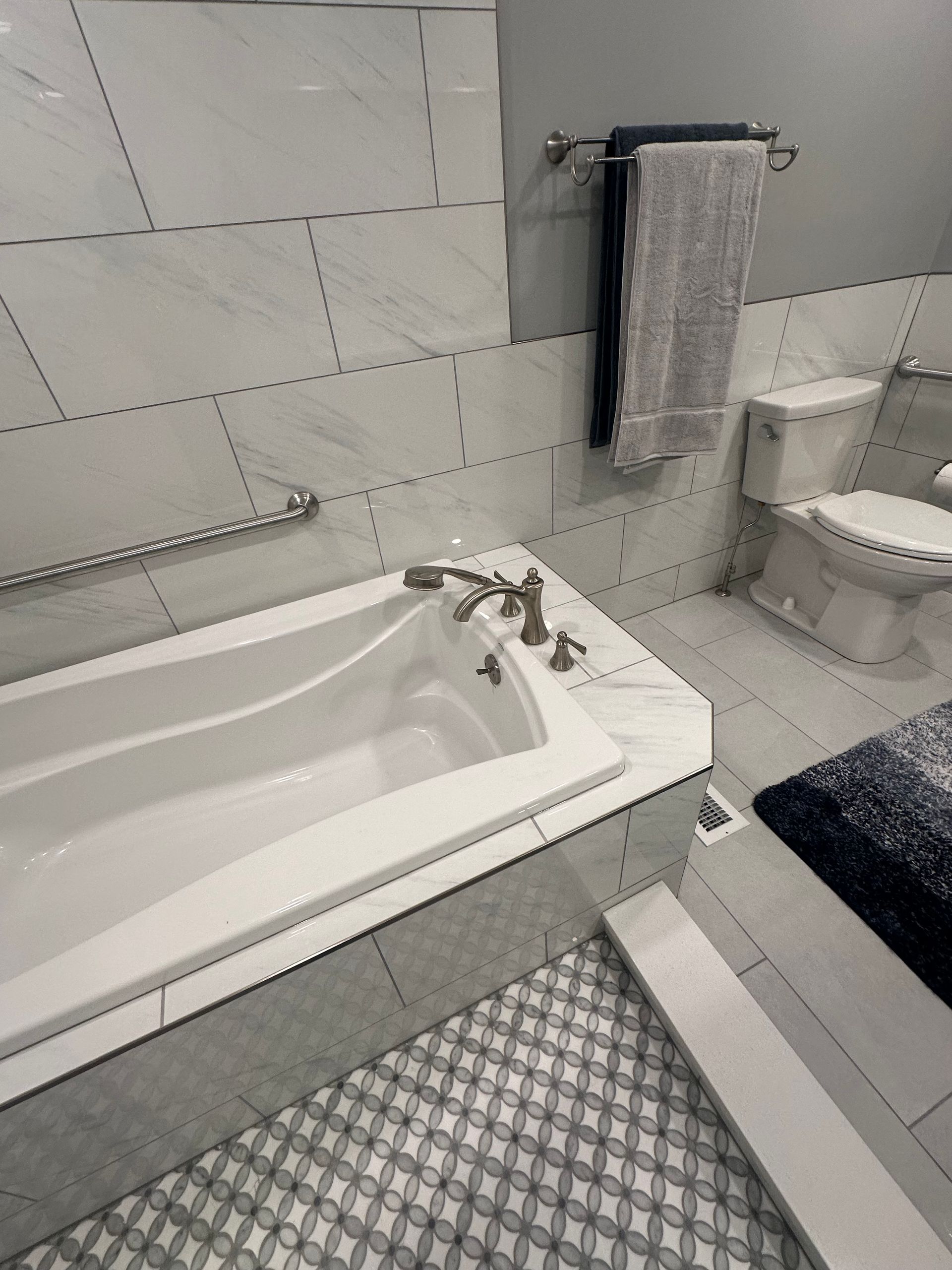 Accessible bathroom with a walk-in tub, grab bars, towel rack, and toilet.