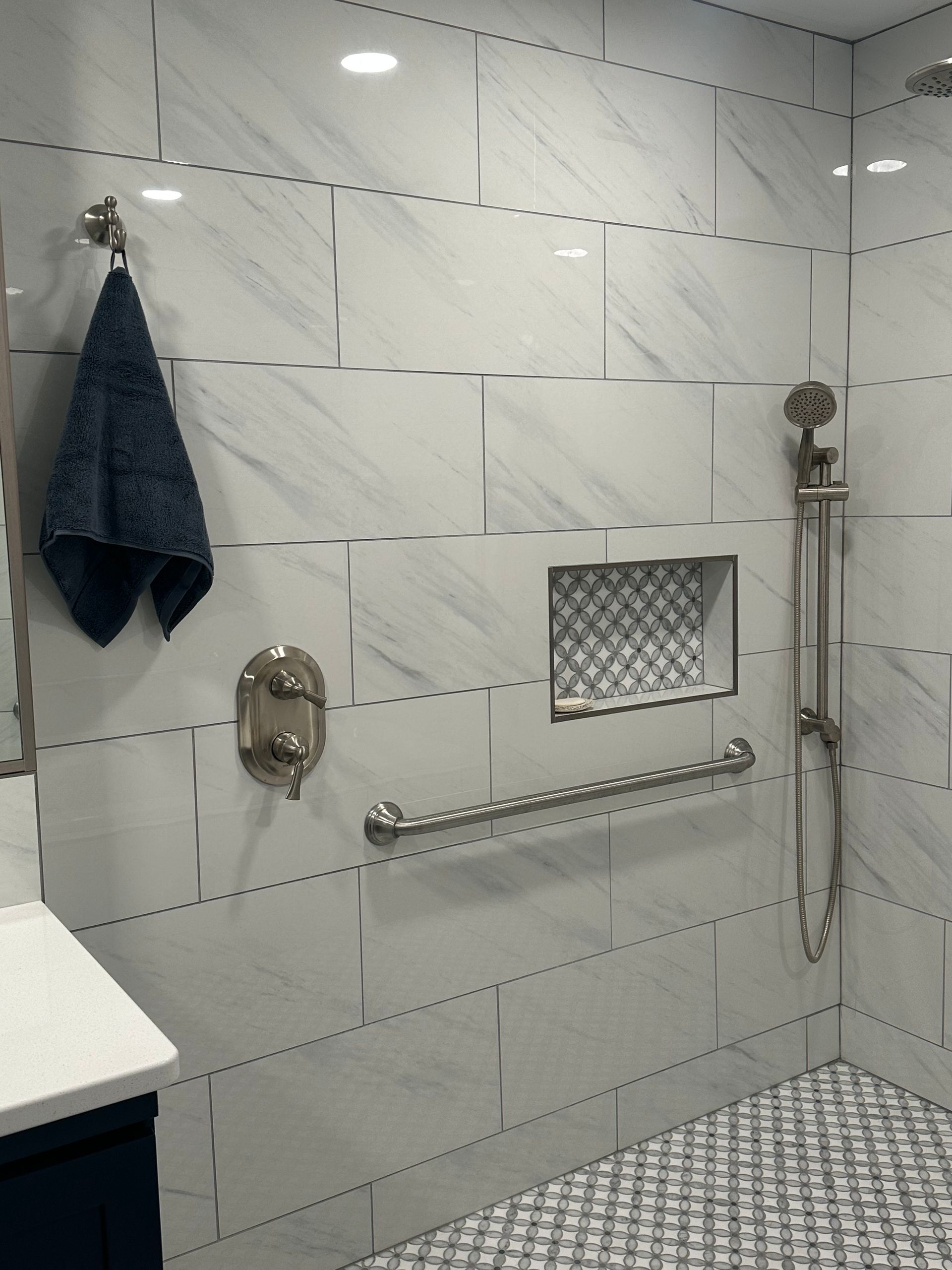 Tiled walk-in shower with grab bar, handheld showerhead, bench, and dark towel hanging on the wall