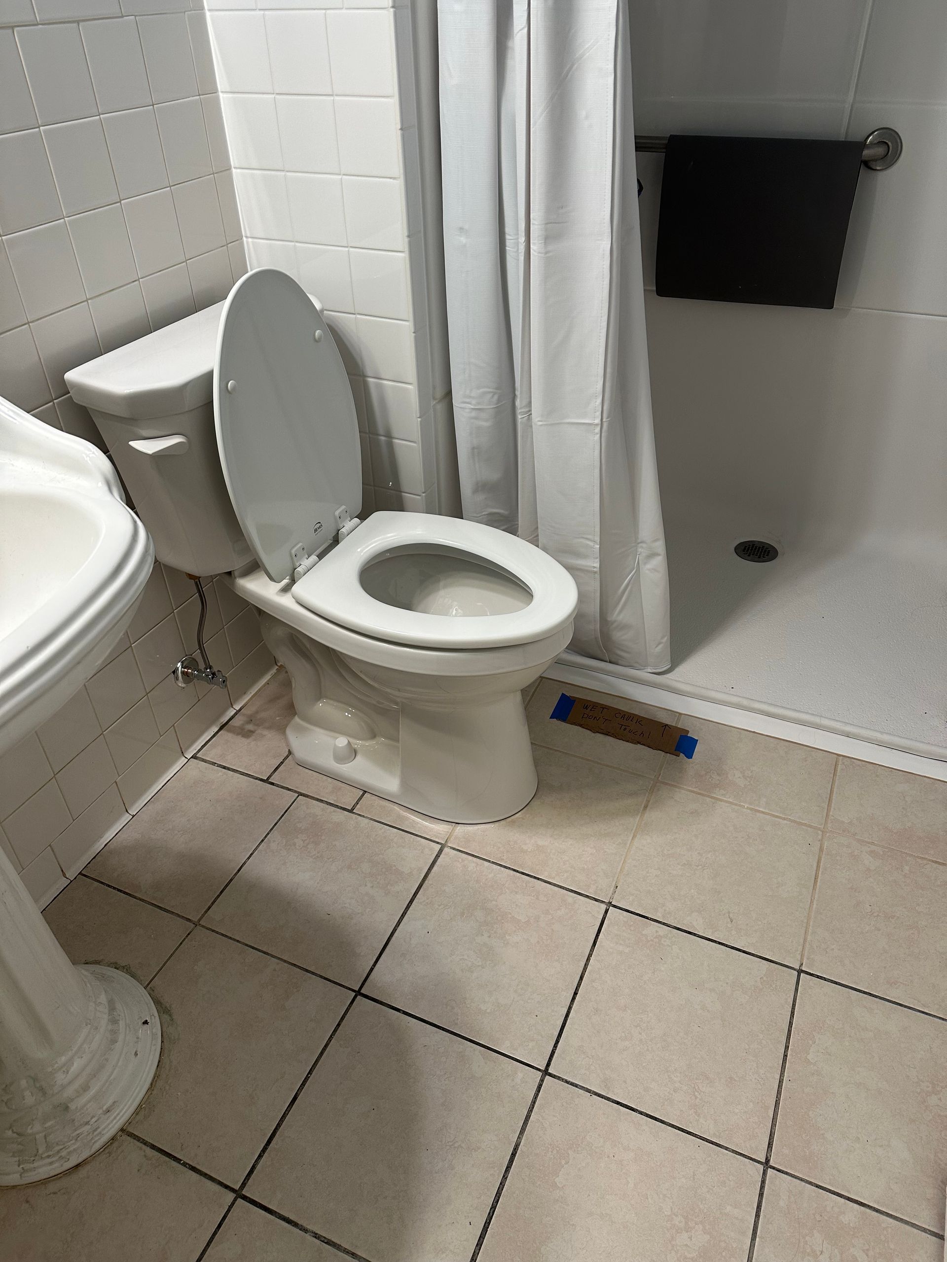 Bathroom with toilet beside a shower stall, white tile walls, and beige floor tiles.