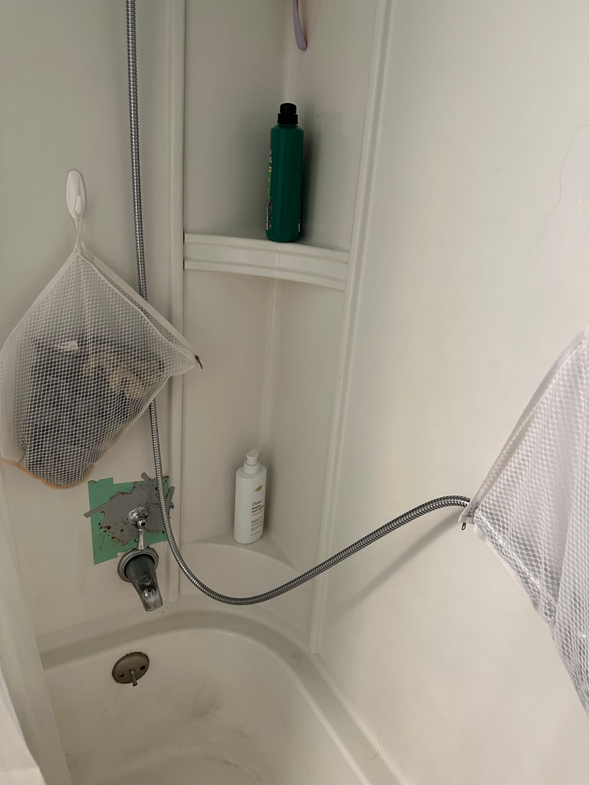 Small bathroom with shower caddy, hanging mesh bags, and a flexible shower hose over a tub.