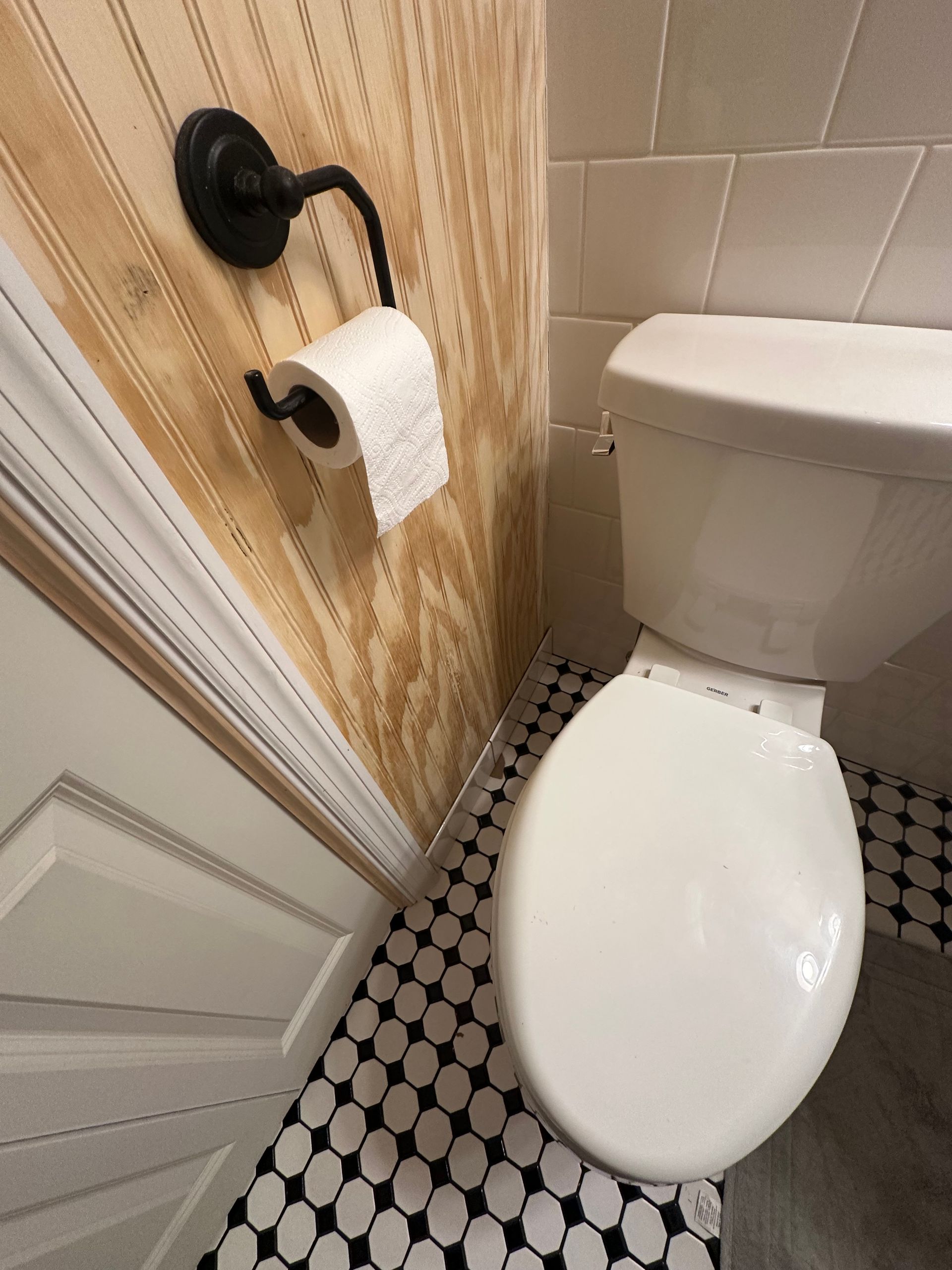 Small bathroom with toilet, patterned black-and-white floor, and a toilet paper holder on striped wallpaper.
