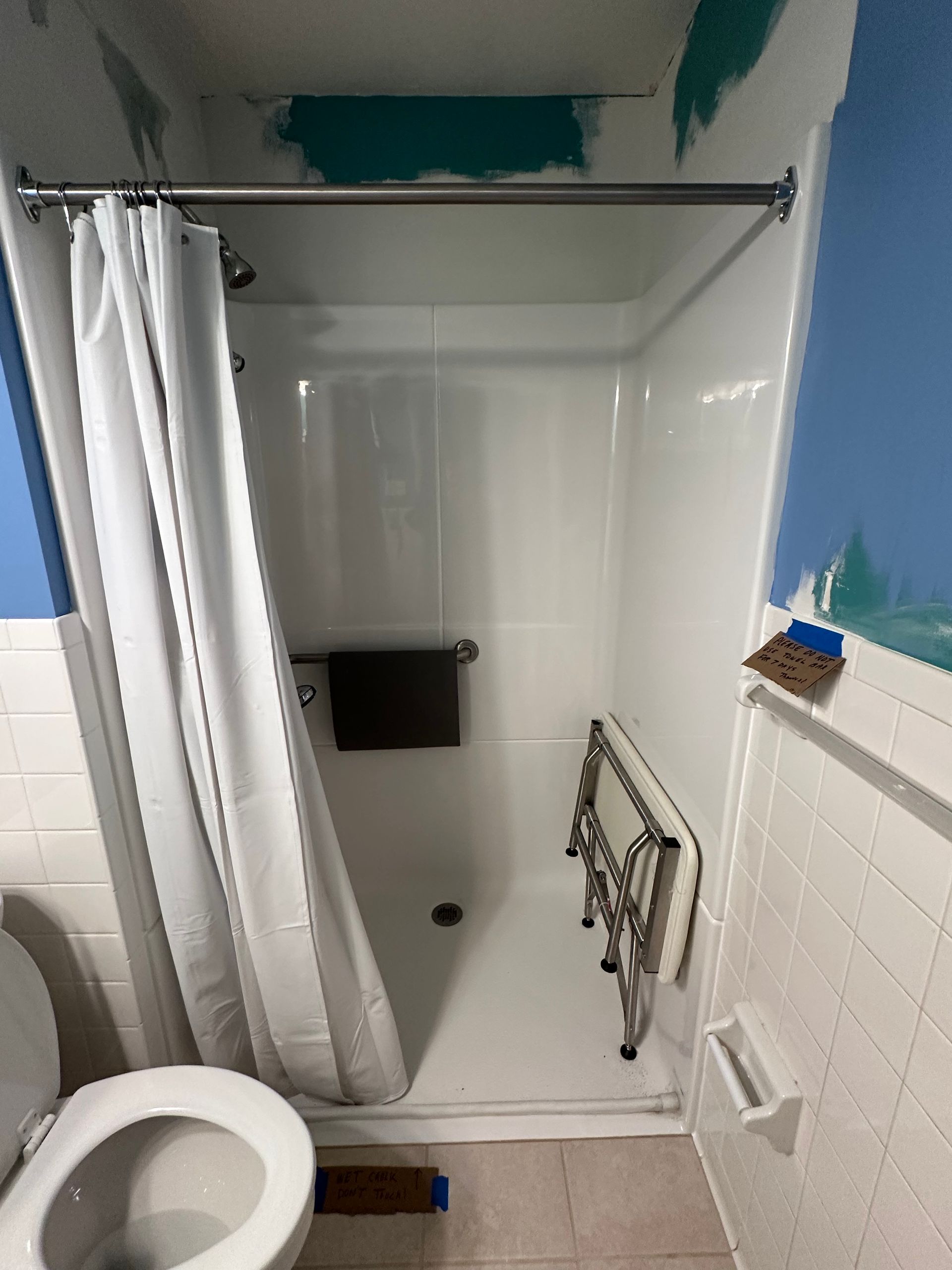 Small bathroom with a white shower/tub, curtain, toilet, and unfinished wall patches.