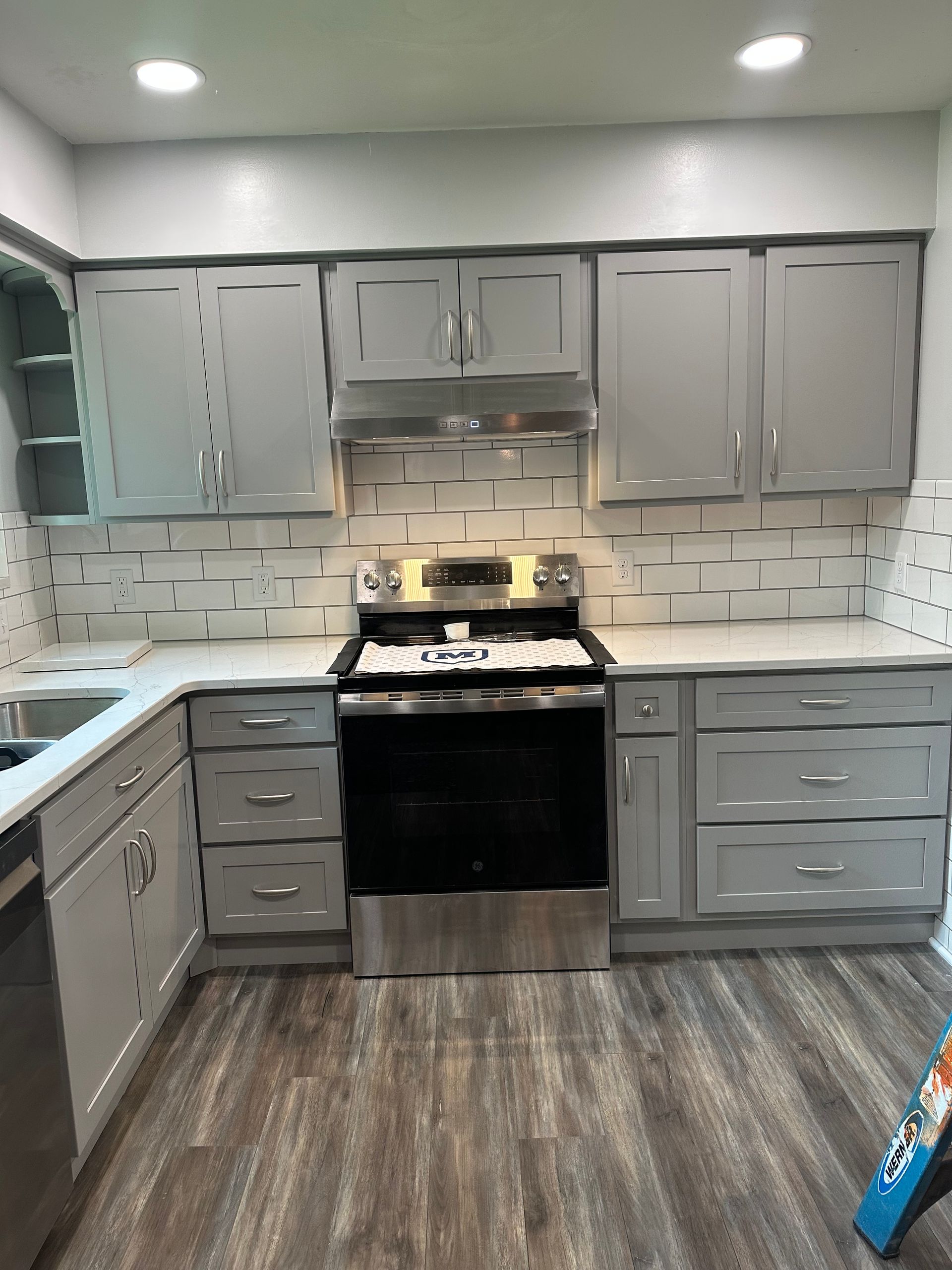 Modern kitchen with gray cabinets, stainless-steel appliances, white tile backsplash, and wood-look flooring