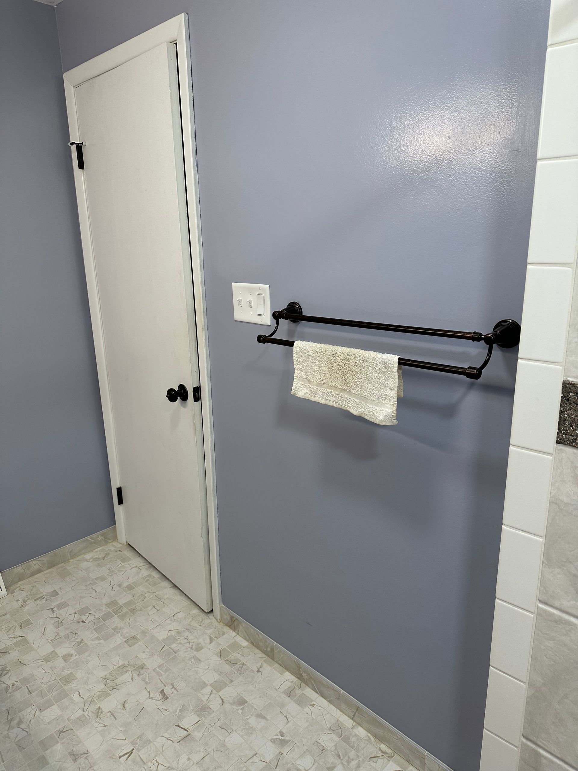 Empty bathroom with lavender wall, white door, towel bar, and tiled floor.