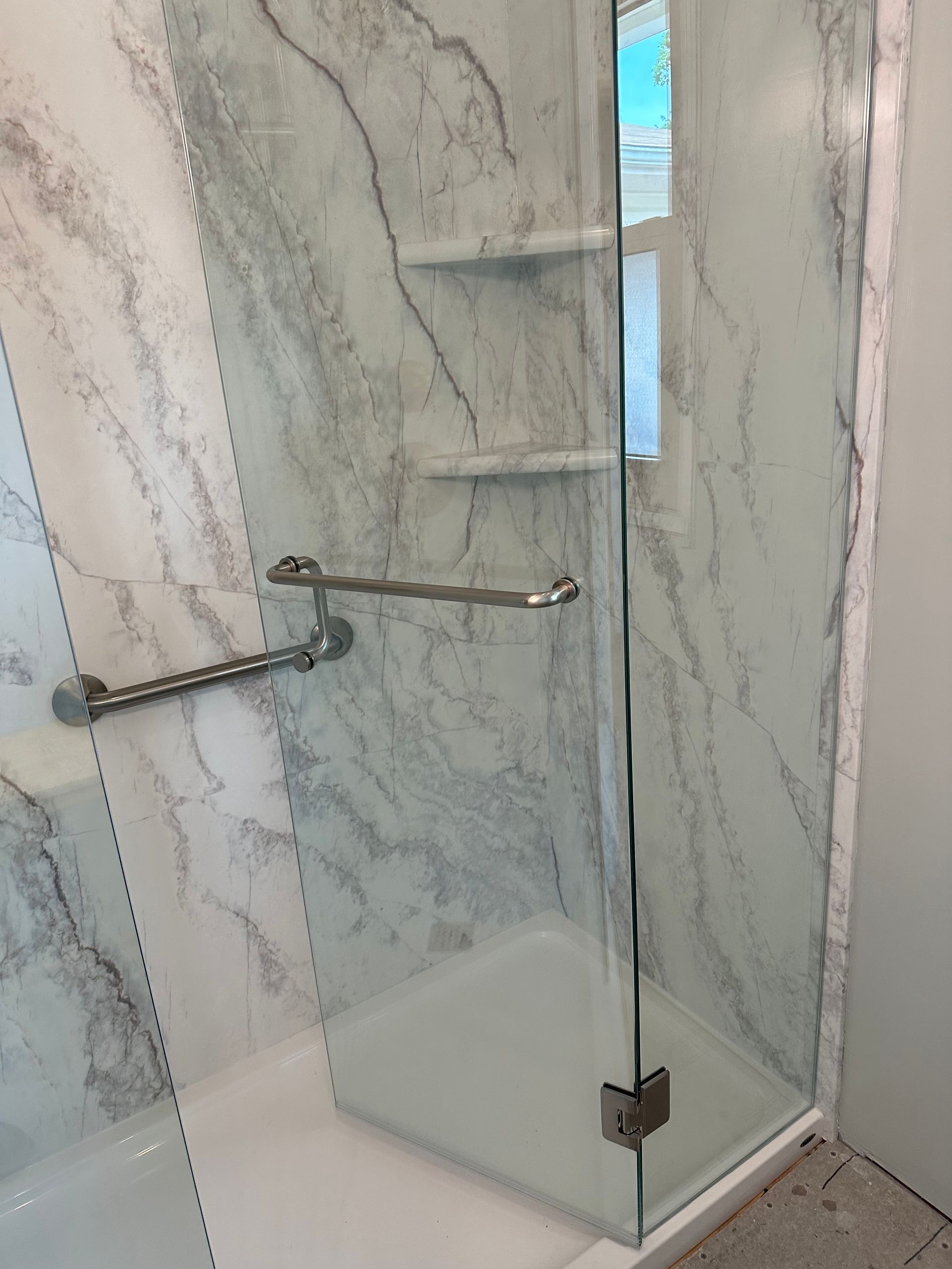 Glass walk-in shower with marble tile walls and chrome grab bars