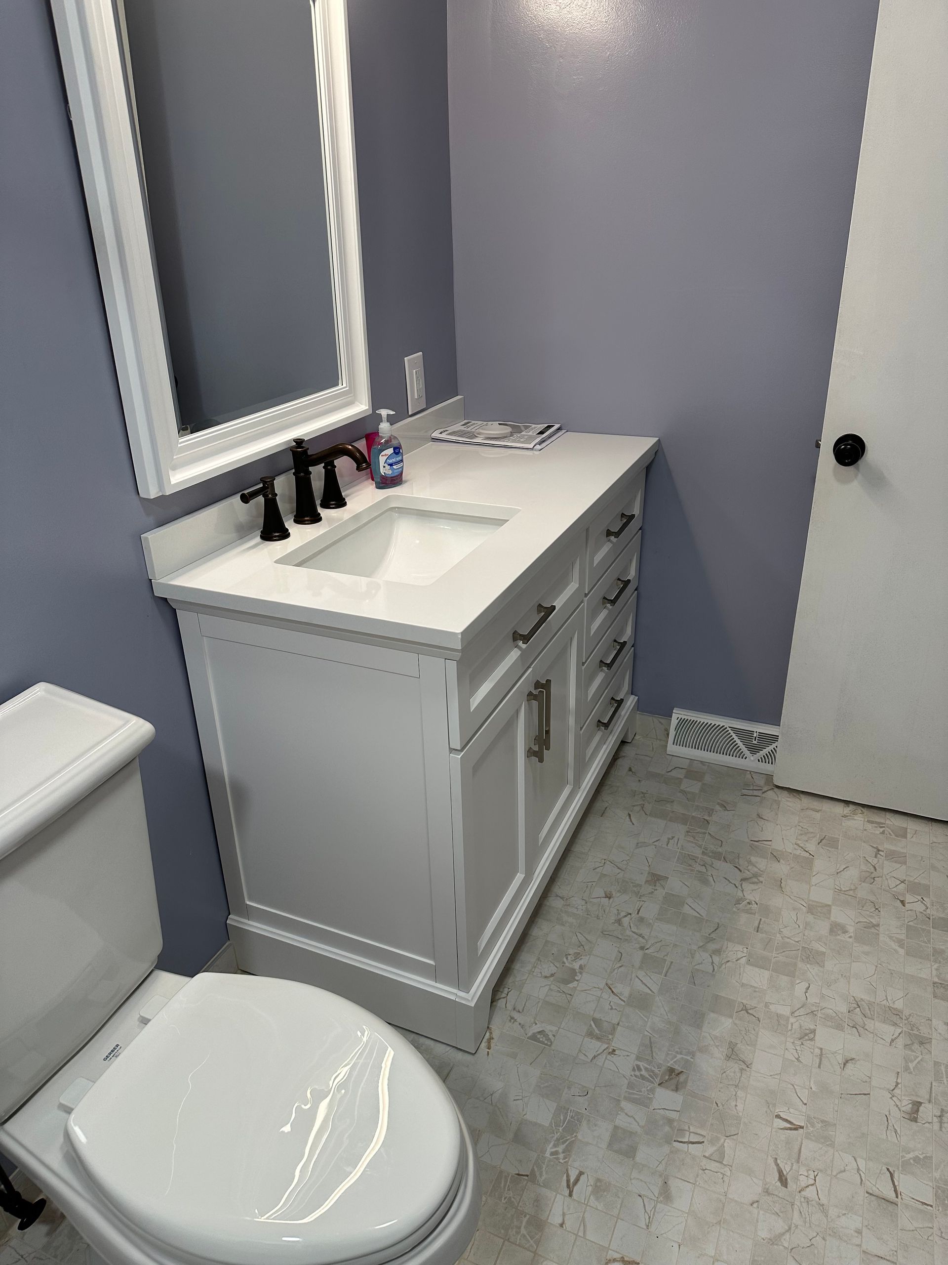 Small bathroom with white vanity, sink, mirror, toilet, and gray walls.