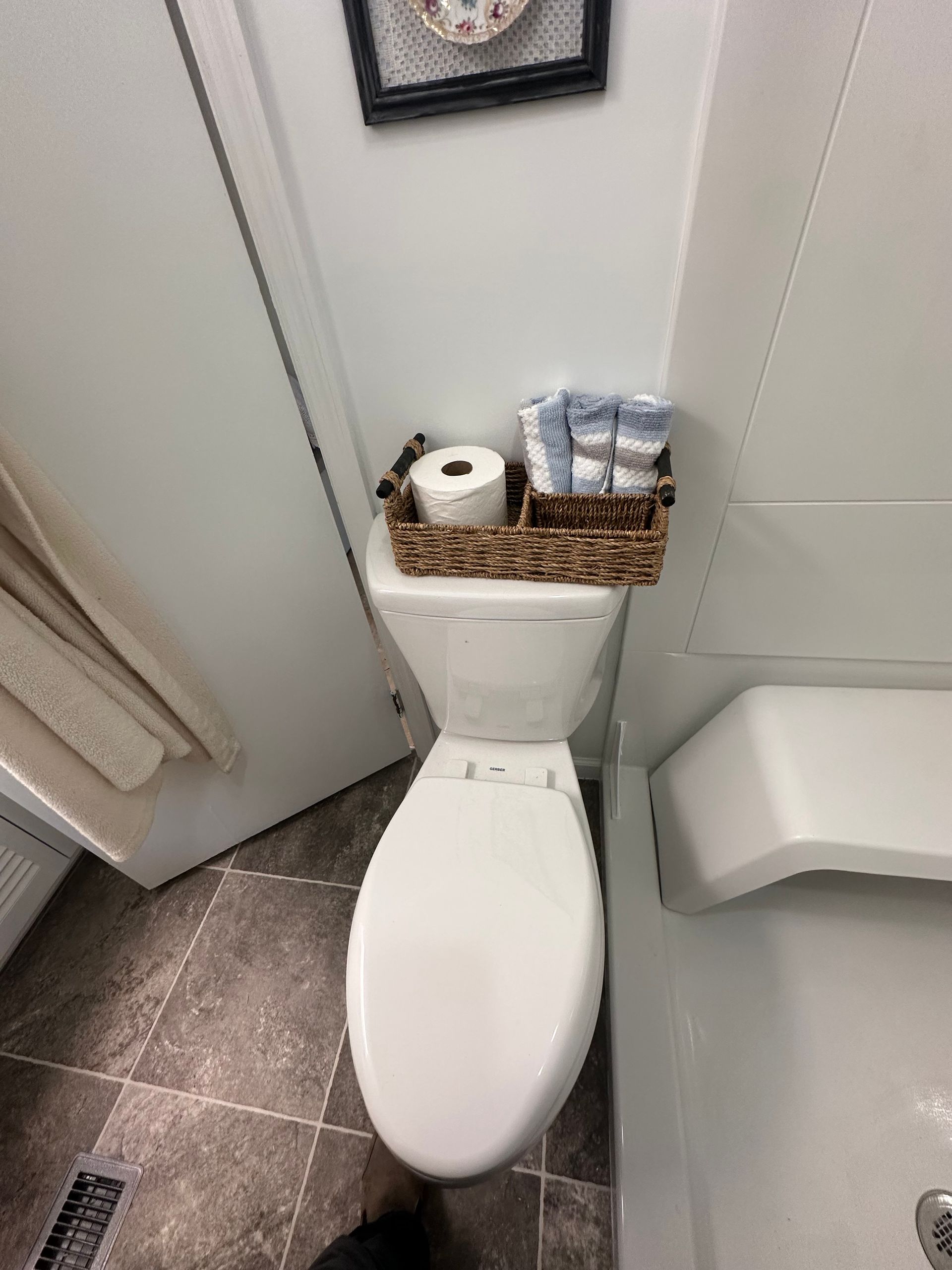 Small bathroom with a toilet topped by a wicker tray holding toilet paper and toiletries.