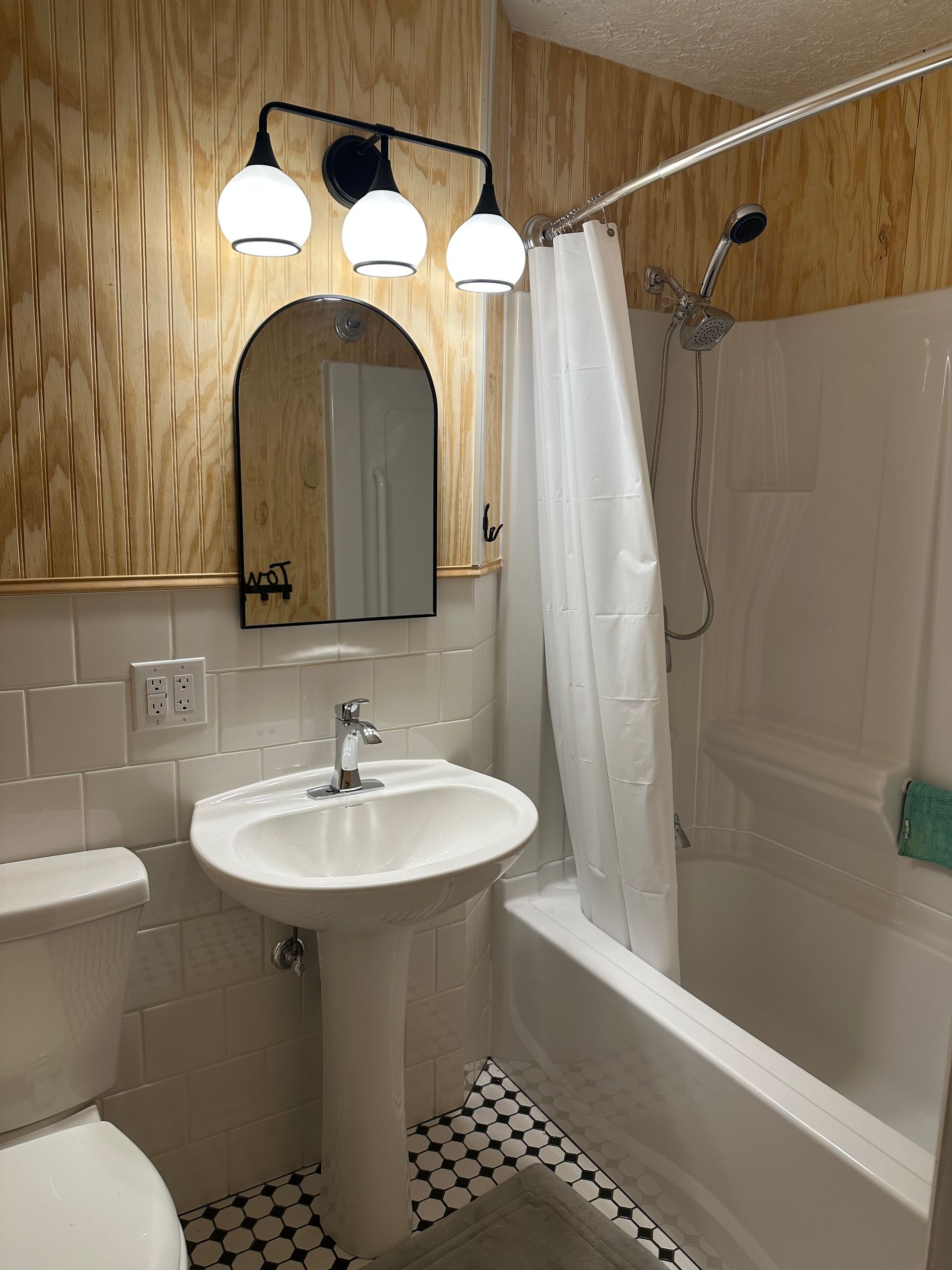 Small bathroom with pedestal sink, mirror lights, shower curtain, and black-and-white tile floor.