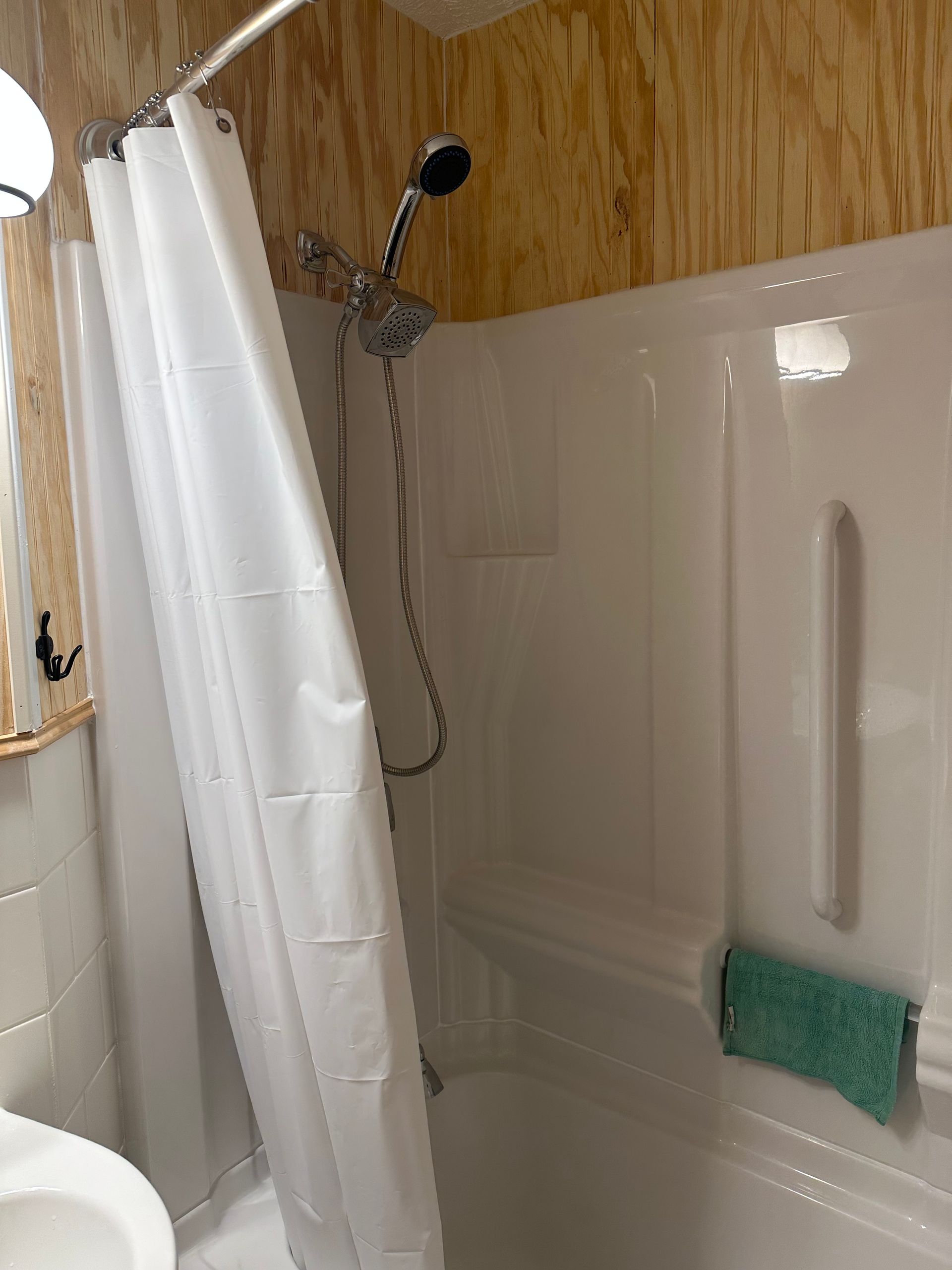 Small shower stall with white walls, a curtain, handheld showerhead, and green scrub pad on the seat.