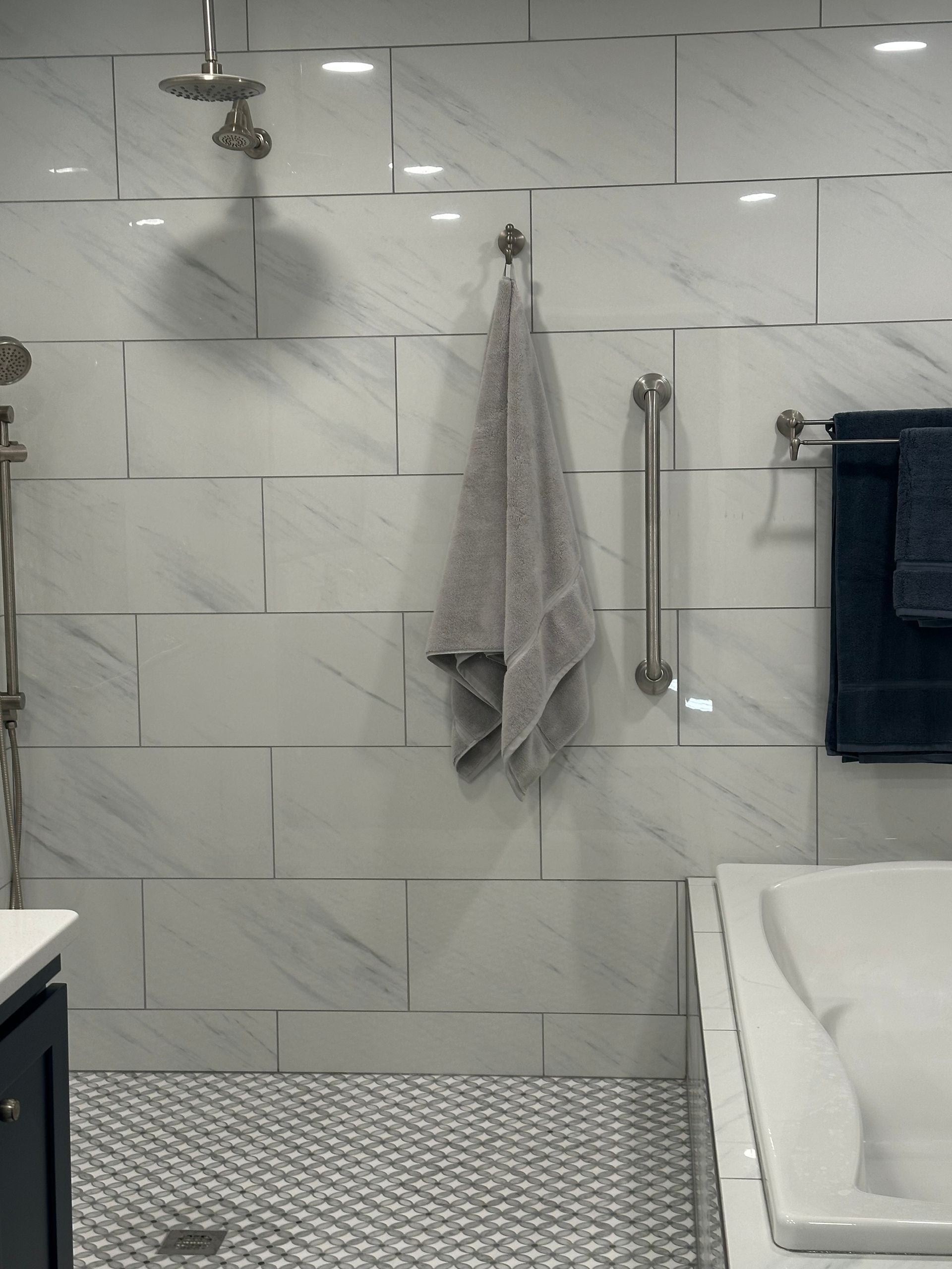 Modern bathroom with white tiled shower wall, towel, grab bar, and shower bench