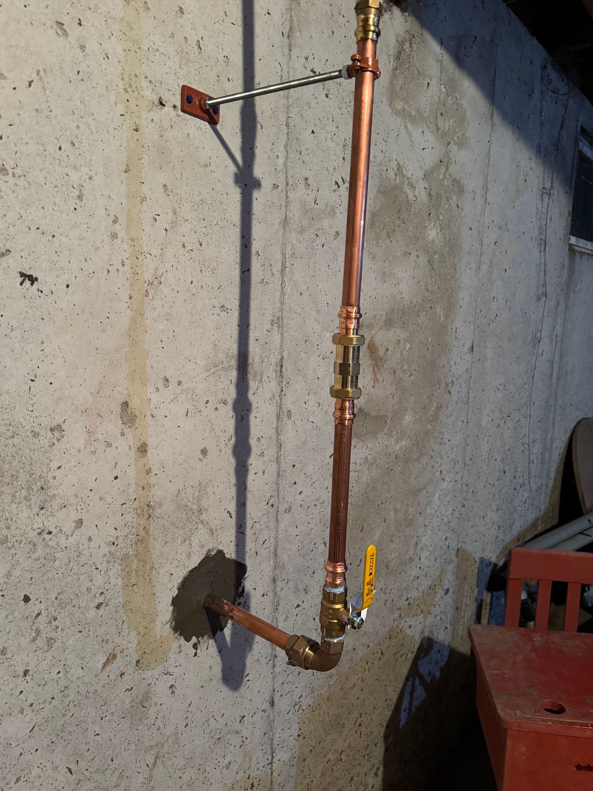 Copper pipe plumbing mounted on a concrete wall, with a shutoff valve and hose connection.