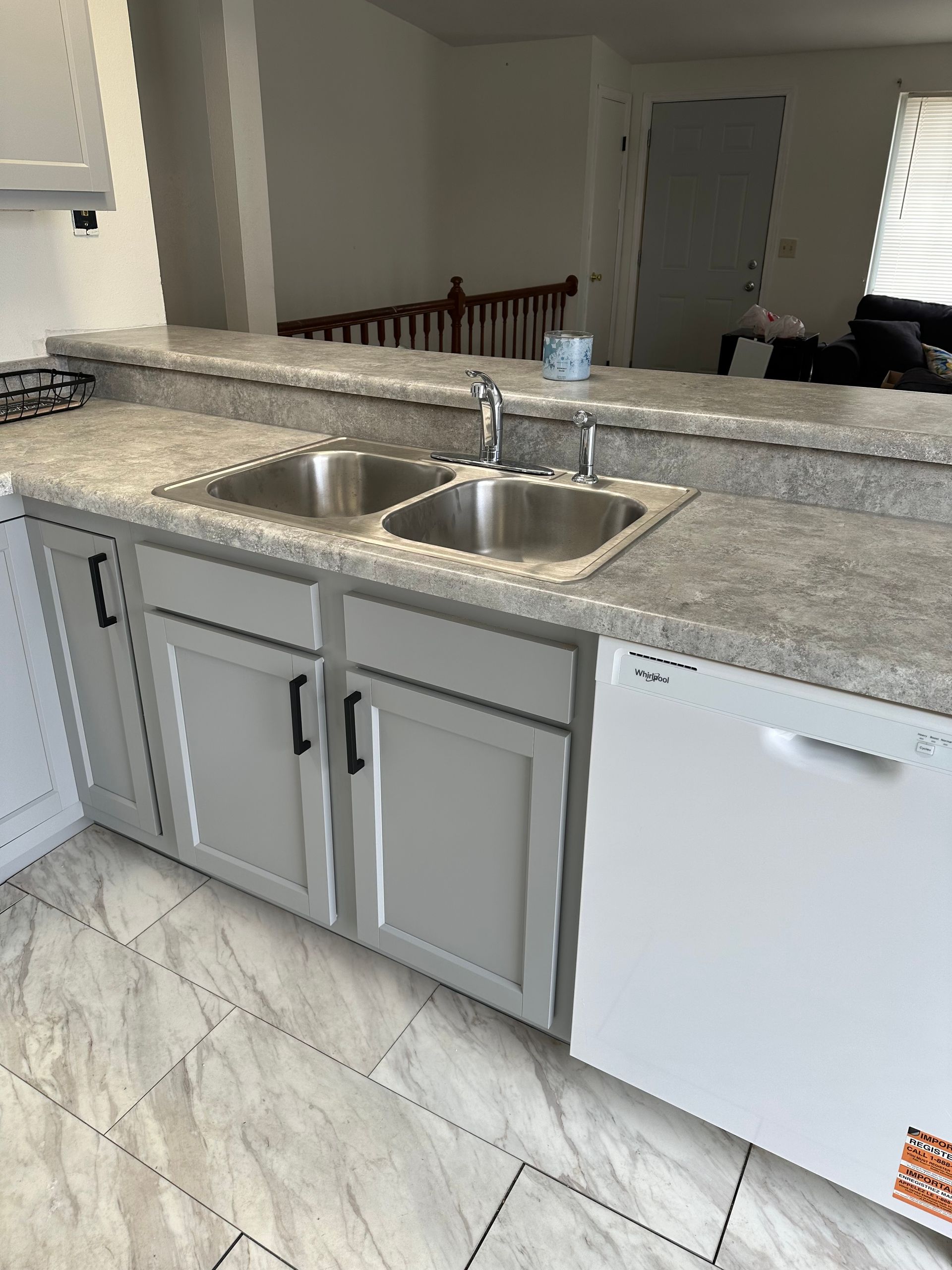 Kitchen sink and granite countertop with gray cabinets and white dishwasher in a bright home kitchen