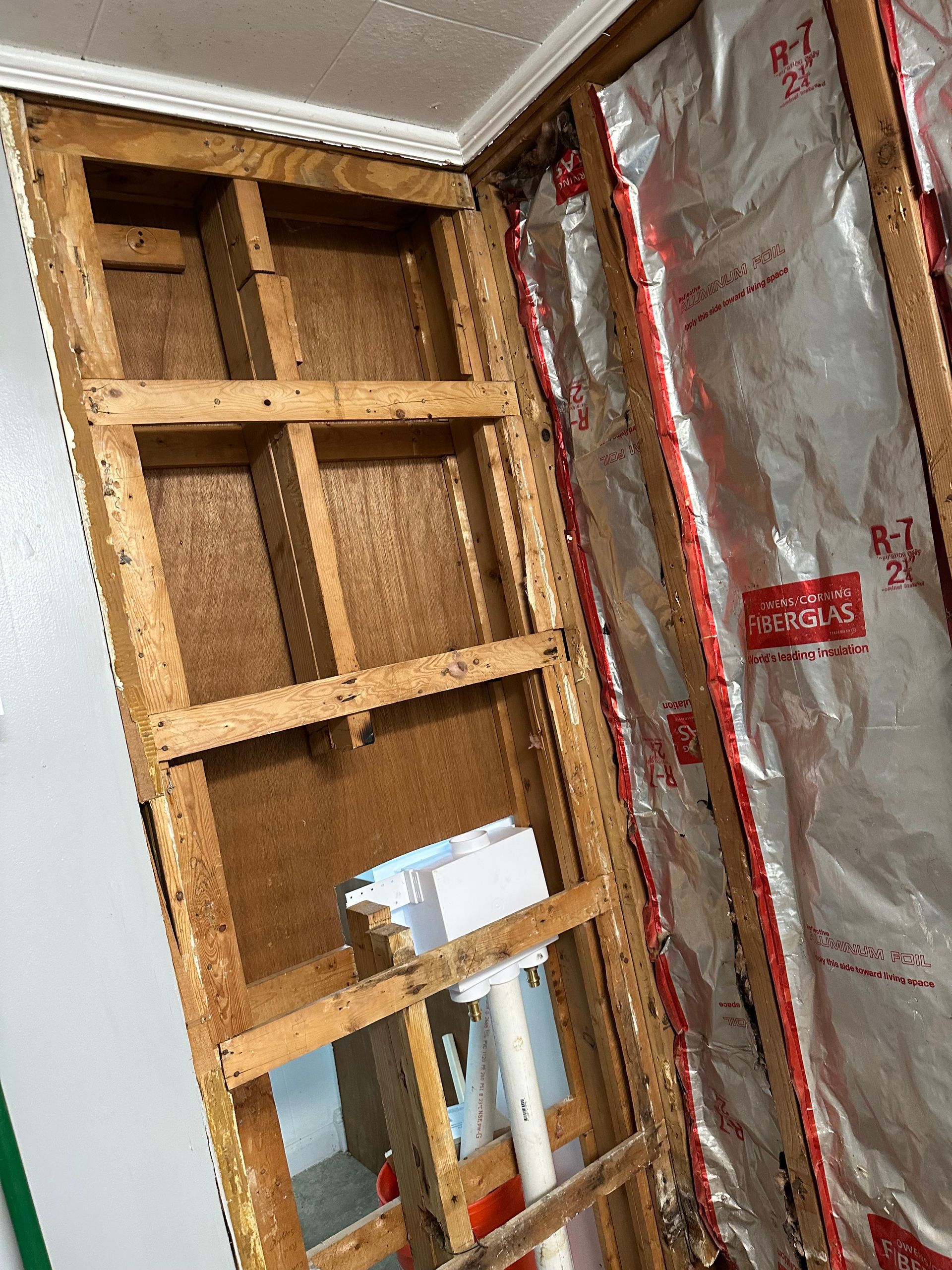 Exposed wall framing beside foil insulation, with a small opening near the floor in an unfinished room