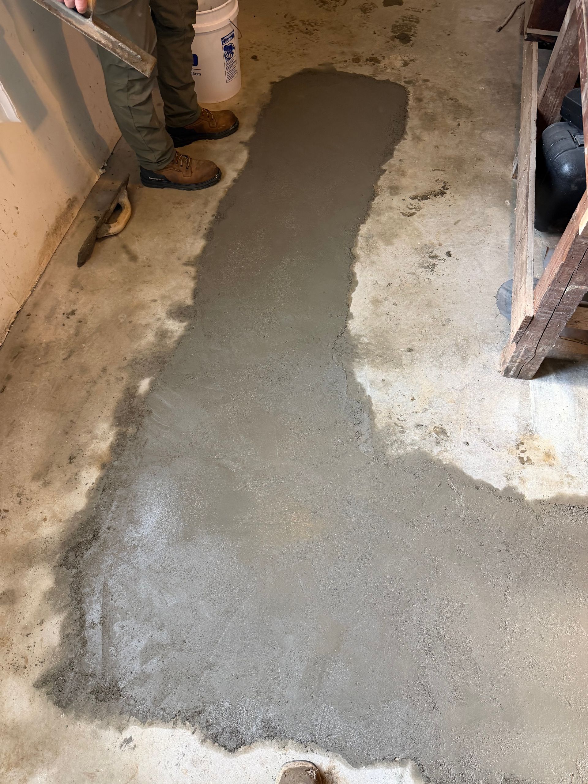 Fresh gray concrete patch on a floor beside unfinished walls and shelving