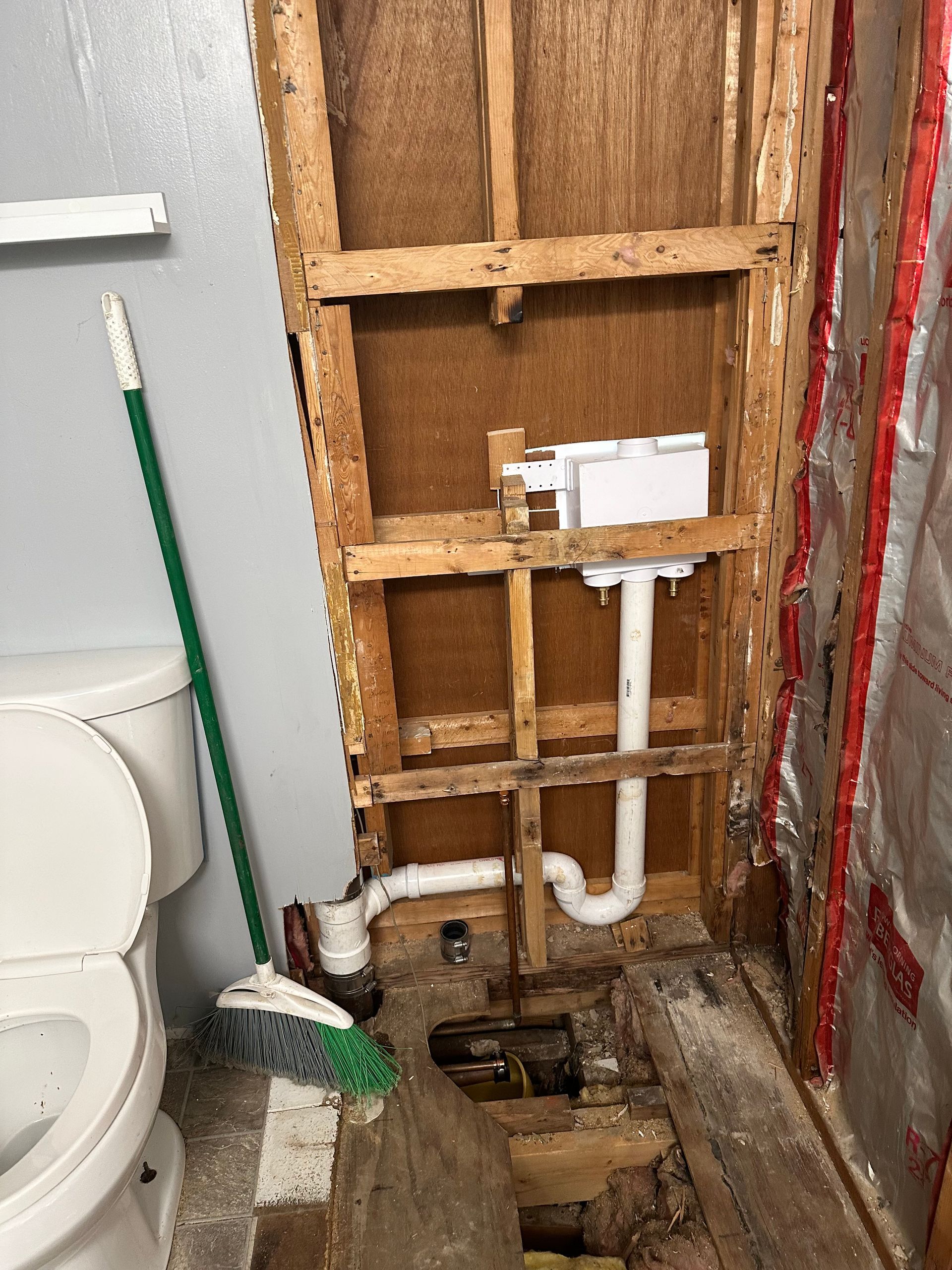 Bathroom wall with exposed plumbing and toilet area under renovation