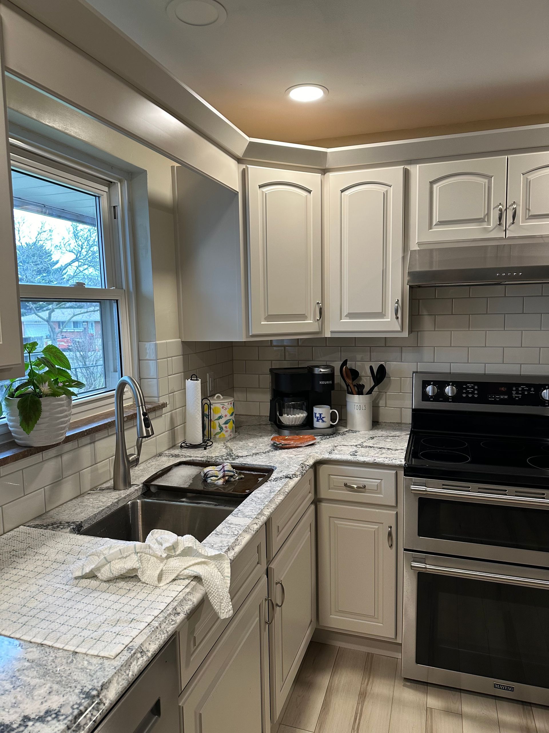 Bright kitchen with white cabinets, granite counters, stainless oven, and a sink by the window.