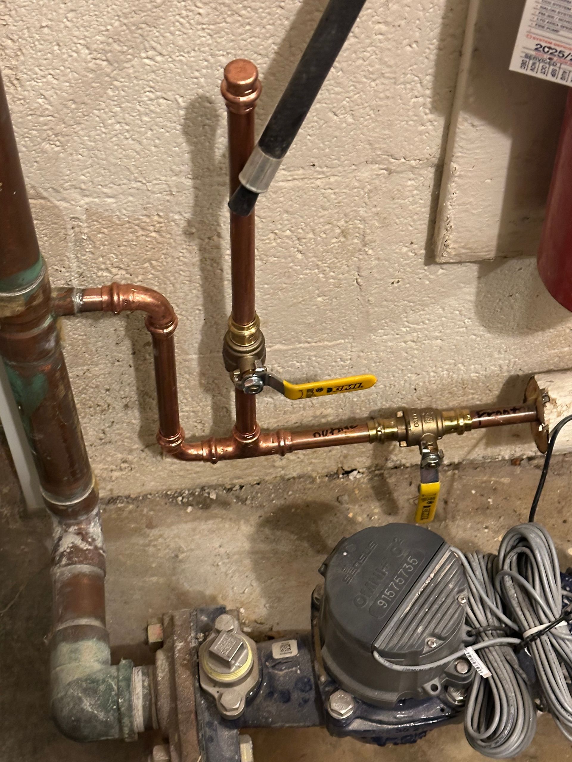 Basement plumbing with copper pipes, shutoff valve, and small pump or compressor unit on a concrete floor