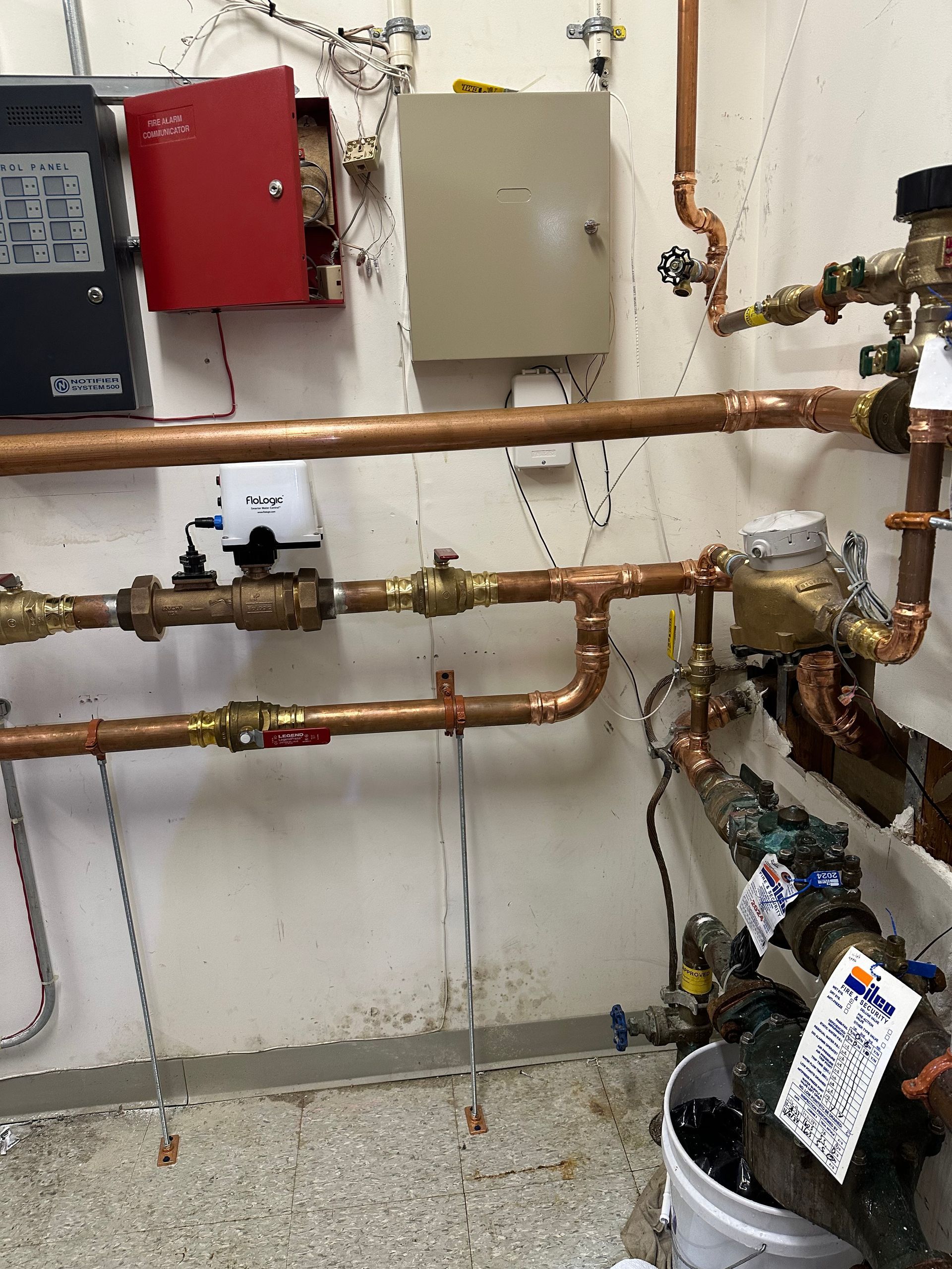 Utility room with exposed copper pipes, valves, meters, and electrical boxes on a white wall