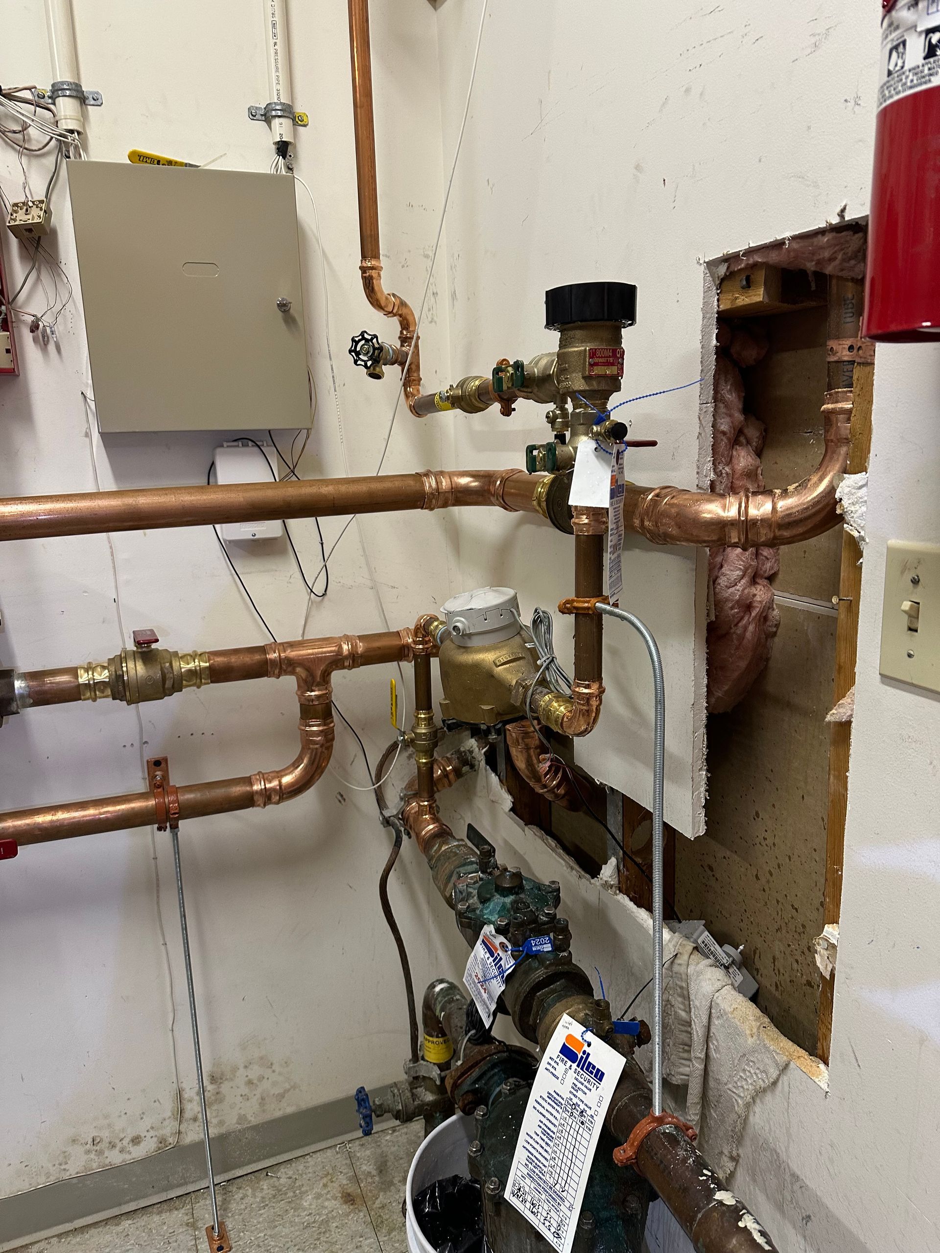 Copper pipes and valves in a utility room, with a small electronic device mounted on the plumbing.