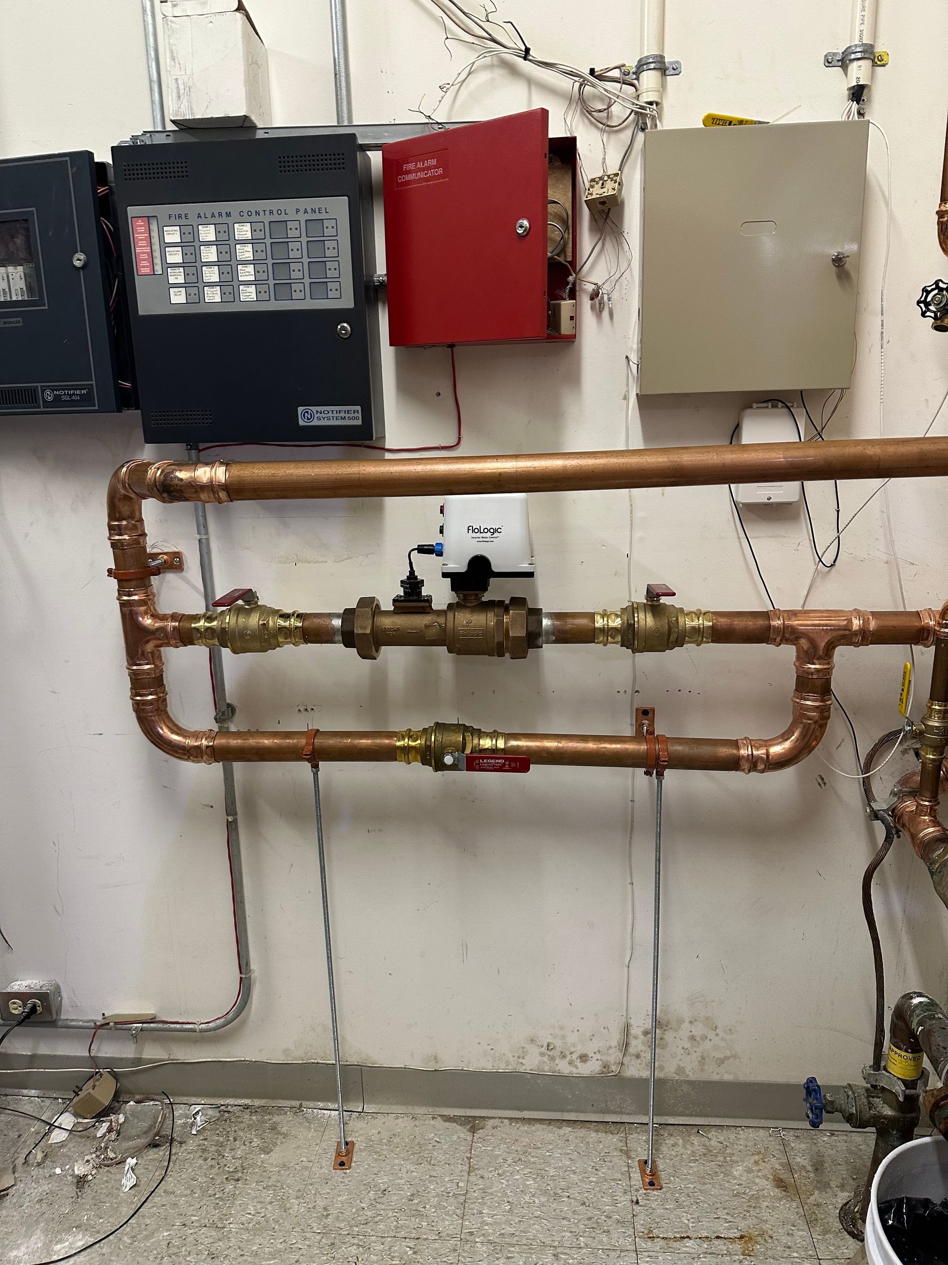 Industrial wall-mounted copper piping and valves beneath electrical control boxes in a utility room