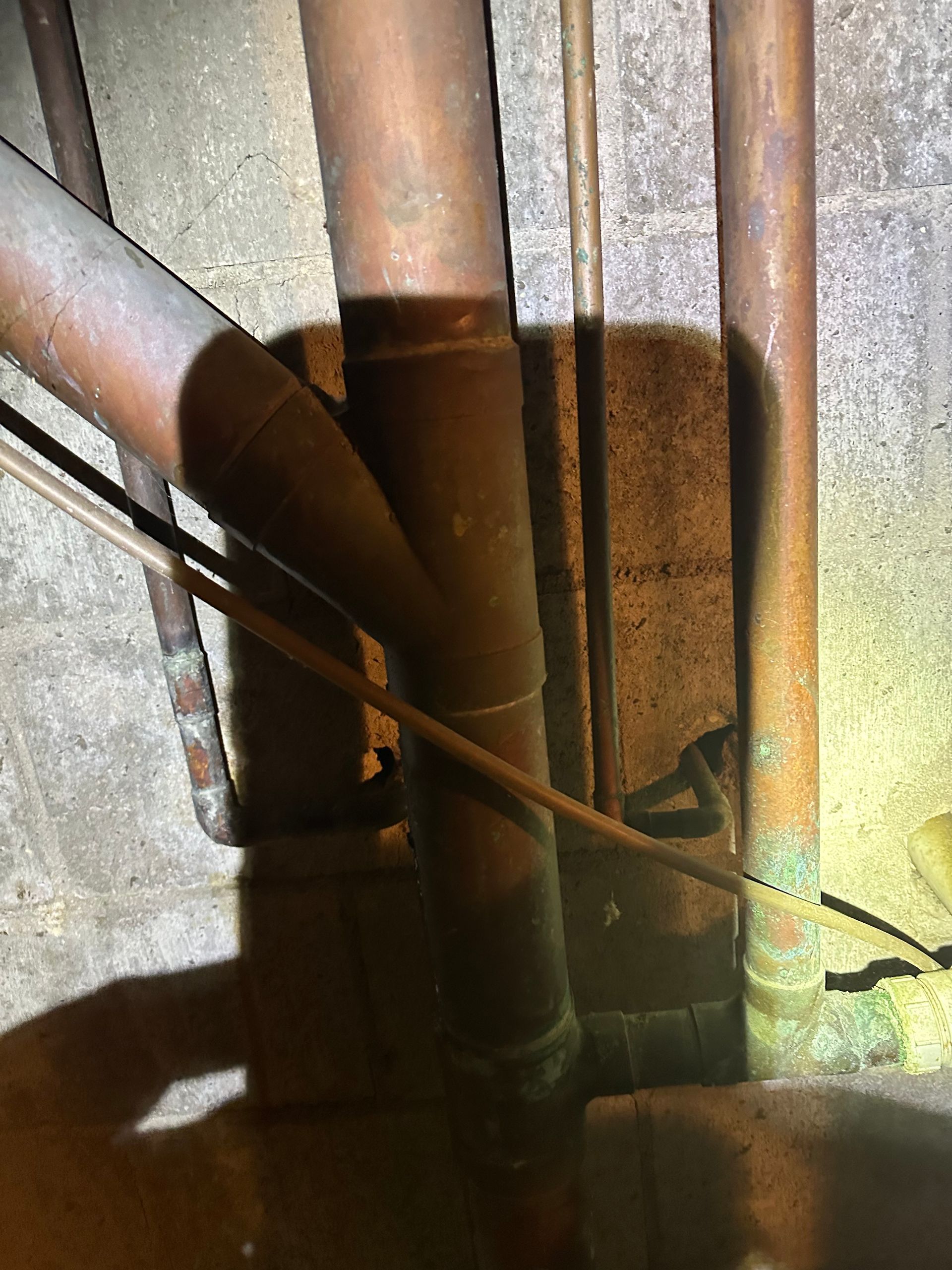 Rusty pipes and cables in a dim utility space against a corrugated metal wall.