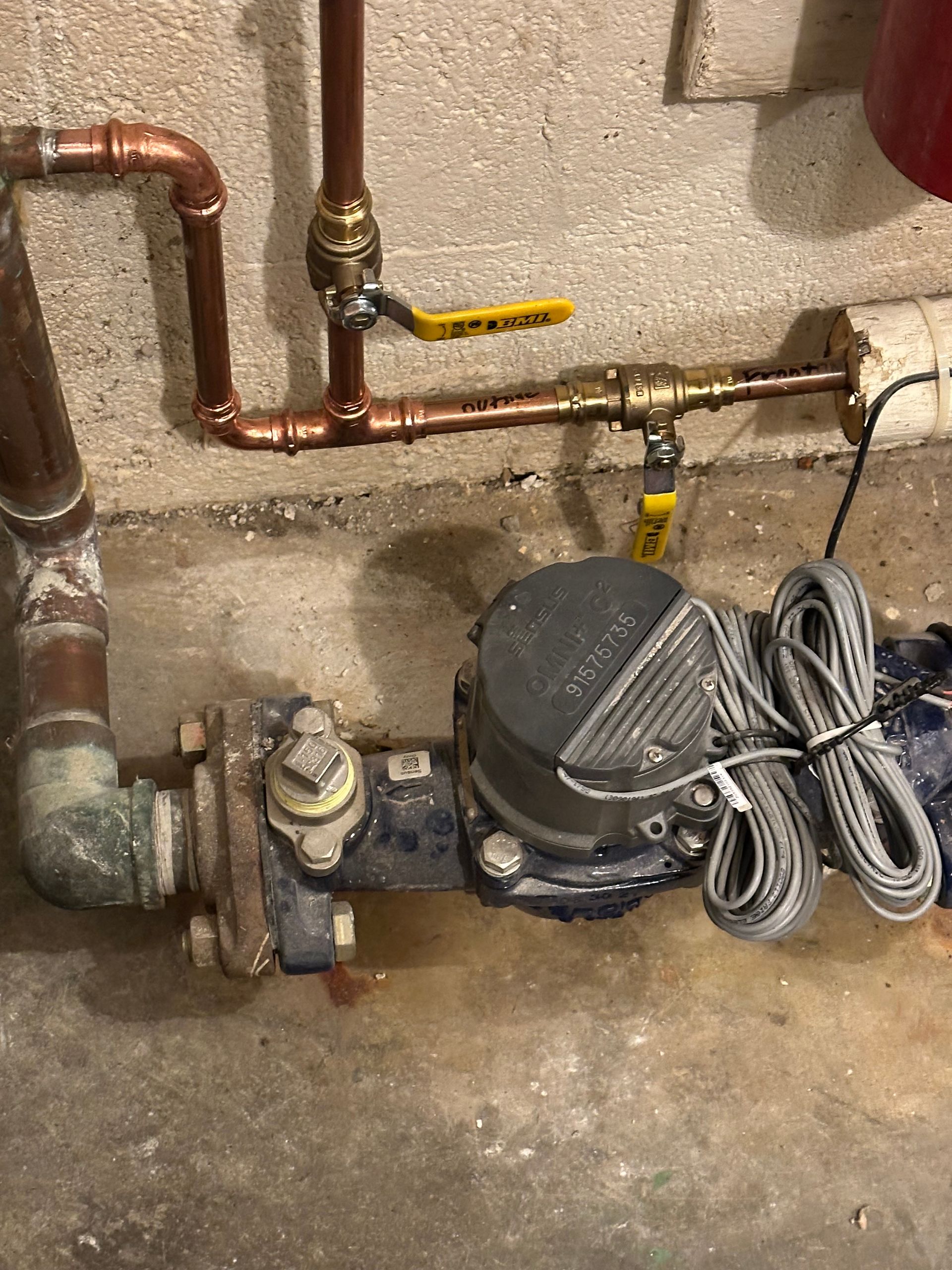 Small basement utility area with a water pump, copper pipes, and yellow shutoff valves on a concrete floor.