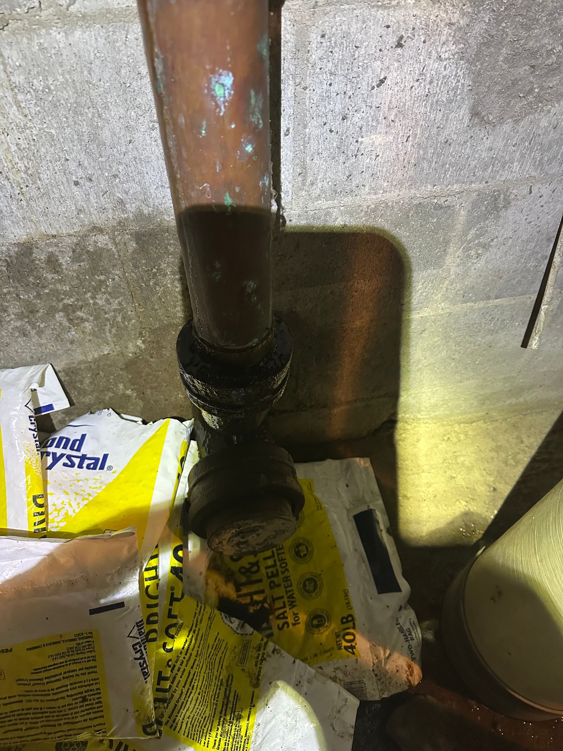 Copper pipe with a dark leak onto yellow bags in a concrete corner, lit by a flashlight